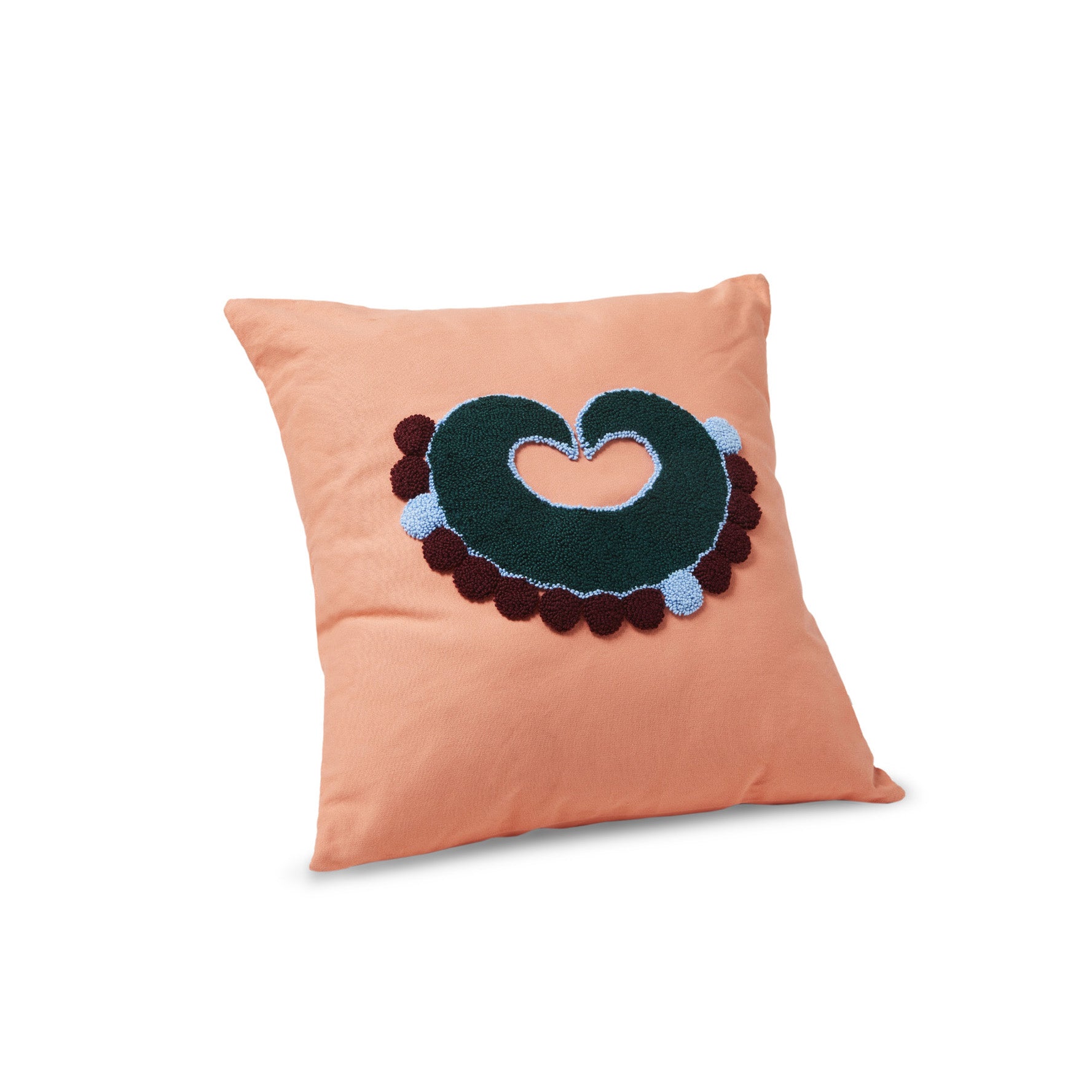 The Nido Piqui cushion from Ames, designed by Sebastian Herkner, features a handmade square design in peach with an abstract green heart at its center. Surrounded by blue and brown circles on a plain white backdrop, it showcases artistic flair typical of the Nido collection.
