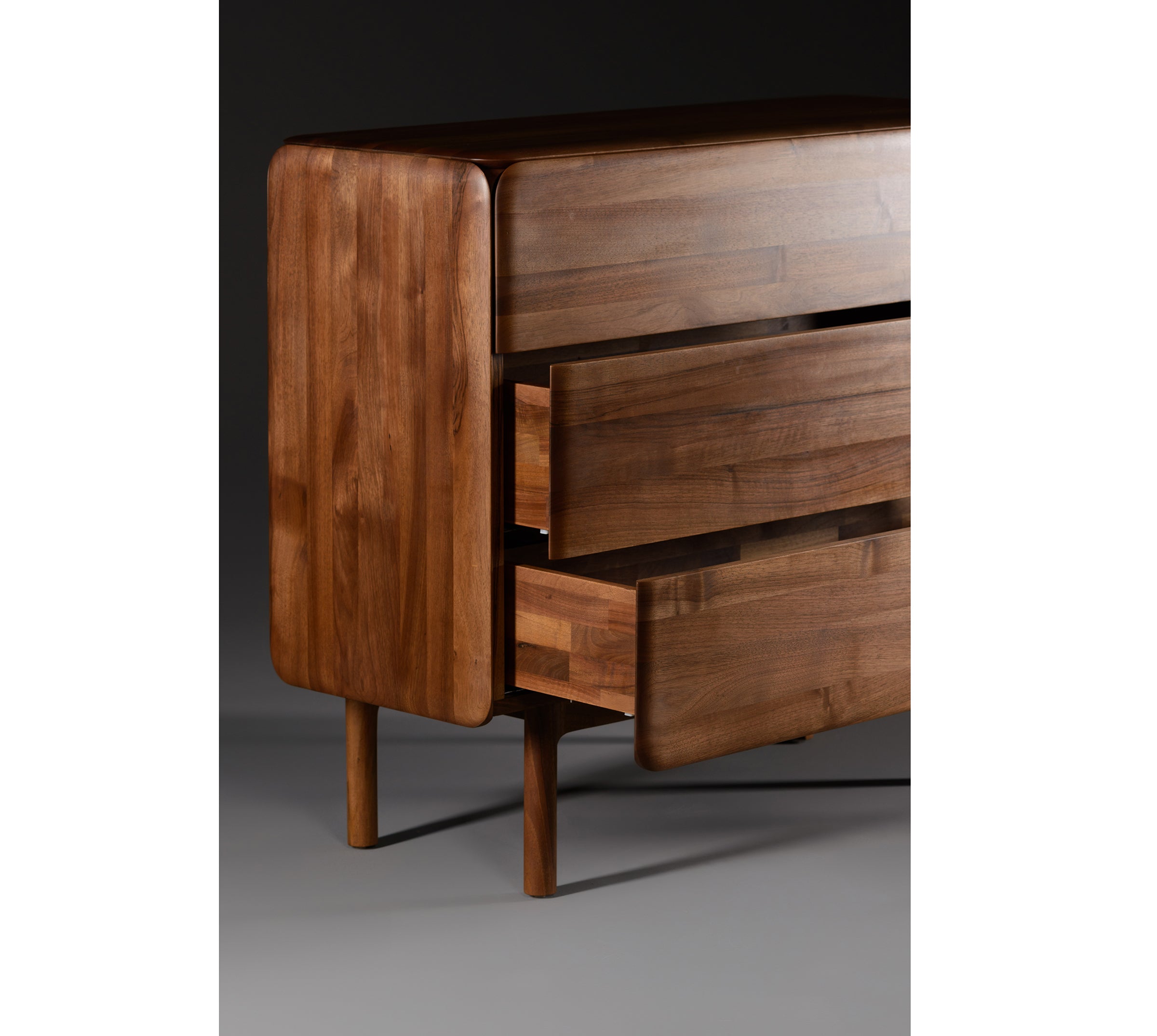The CLOUD High board by Artisan is crafted from solid wood with a smooth, polished finish and natural oils. It features three slightly open drawers, rounded edges, and stands on four slender legs against a dark background.