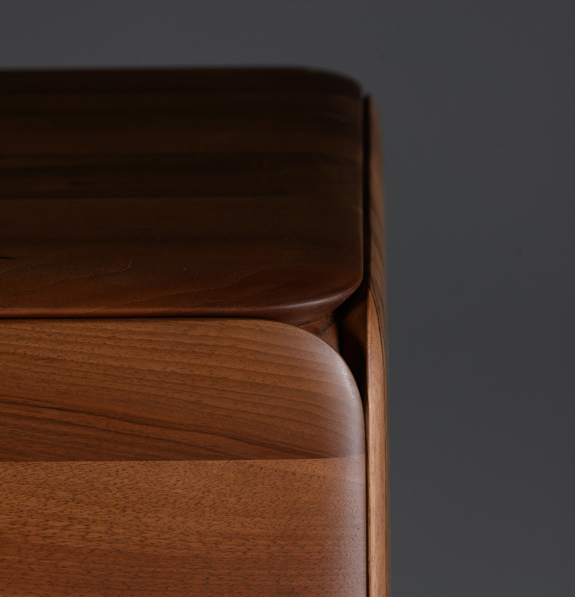 Close-up of a CLOUD High board corner by Artisan against a dark backdrop, displaying smooth, rounded edges and a rich brown finish with visible wood grain, crafted from solid wood and polished with natural oils.