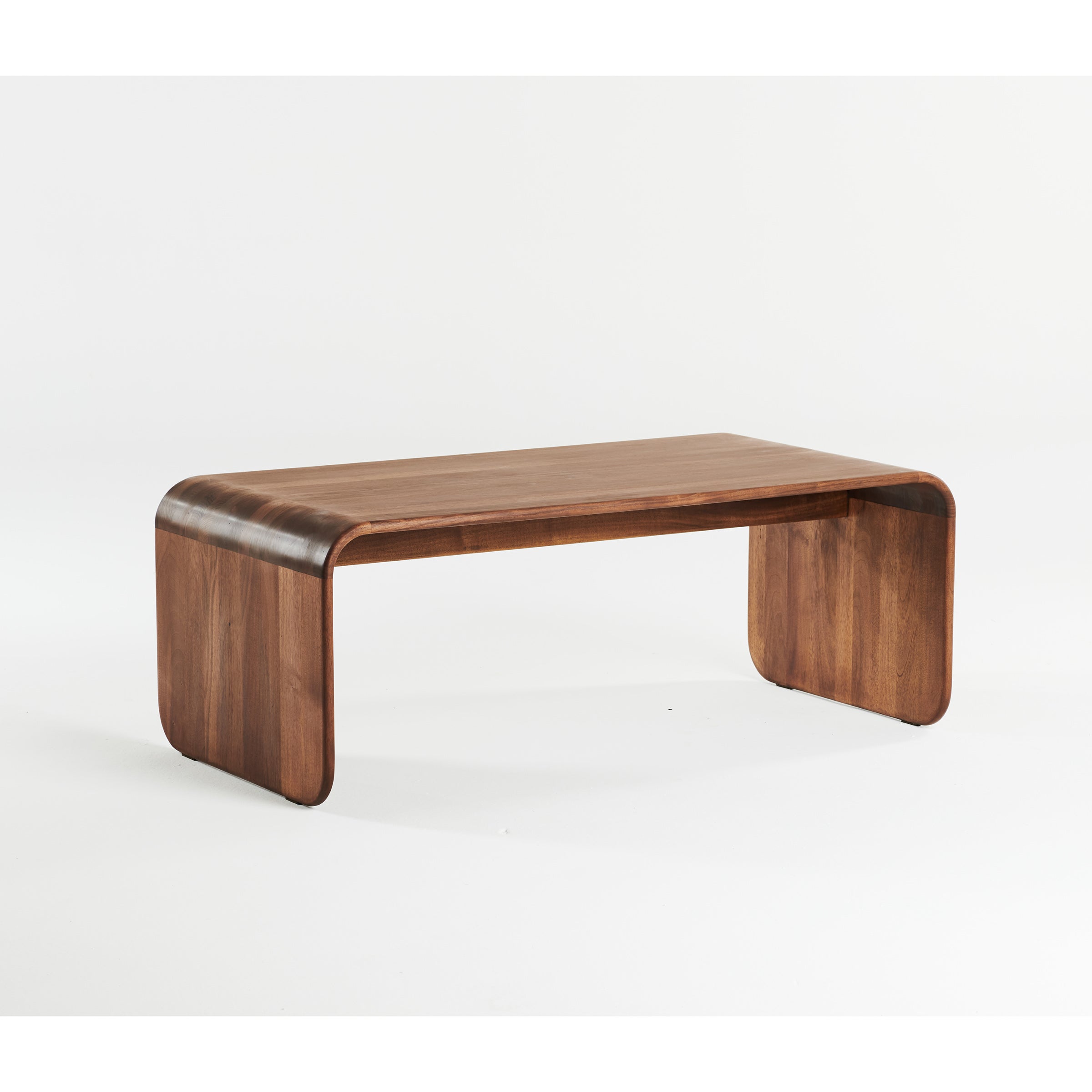 The ENY Coffee Table by Artisan features a sleek and minimalist design. Crafted from solid wood, it has a smooth curved top with rounded edges supported by two flat curved legs, seamlessly blending into the tabletop. It’s finished with natural oils for a warm, rich brown hue.