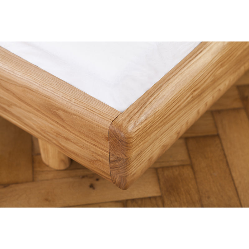 Close-up of Artisans FIN Bed, showcasing its rounded wooden frame crafted from eco-friendly materials. The natural finish highlights the wood grain, enhancing its allure. Resting on a parquet floor, this solid wood bed is topped with a white mattress.