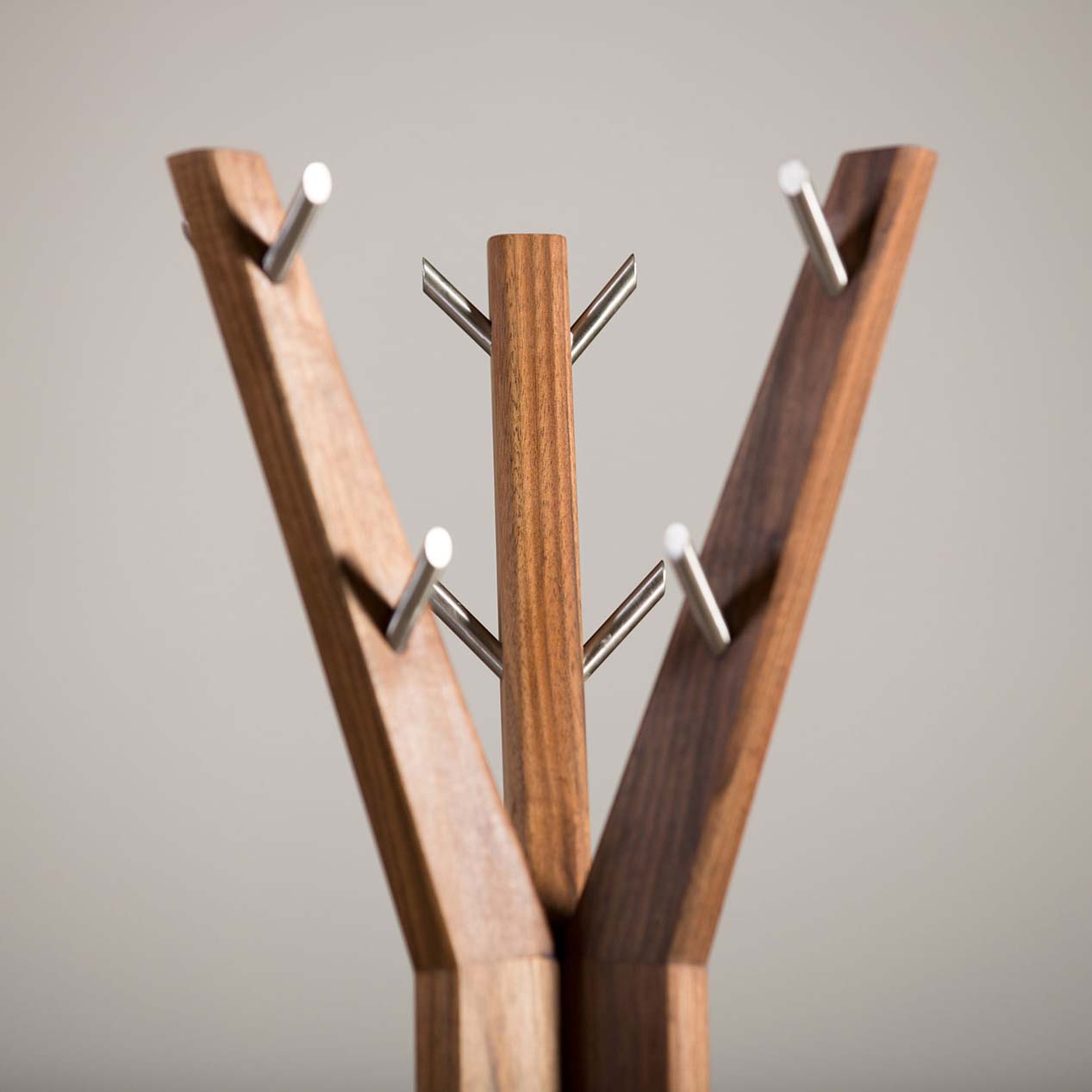 Close-up of the Artisan HANNY Coat Stand, a modern design with three solid wood branches resembling tree limbs. Each branch has multiple metal hooks, and the unit features a rich finish achieved through natural oils against a plain background.