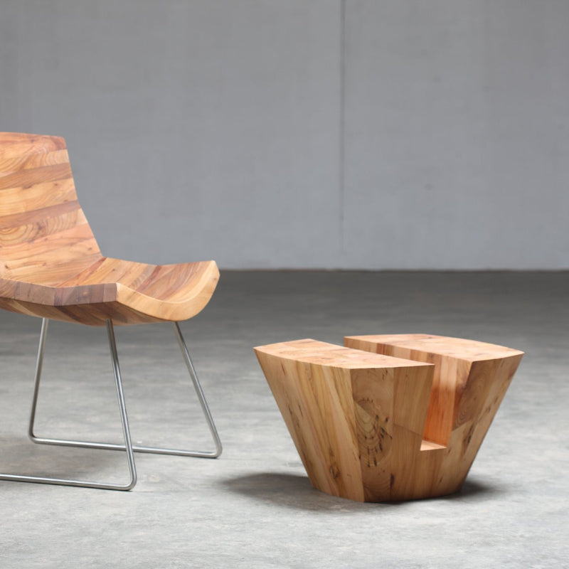 The Artisan KART Coffee Table, featuring a modern geometric design with metal legs and crafted from solid wood polished with natural oils, sits on a gray concrete floor alongside its matching chair. Both pieces showcase smooth finishes and beautiful wood grain patterns.