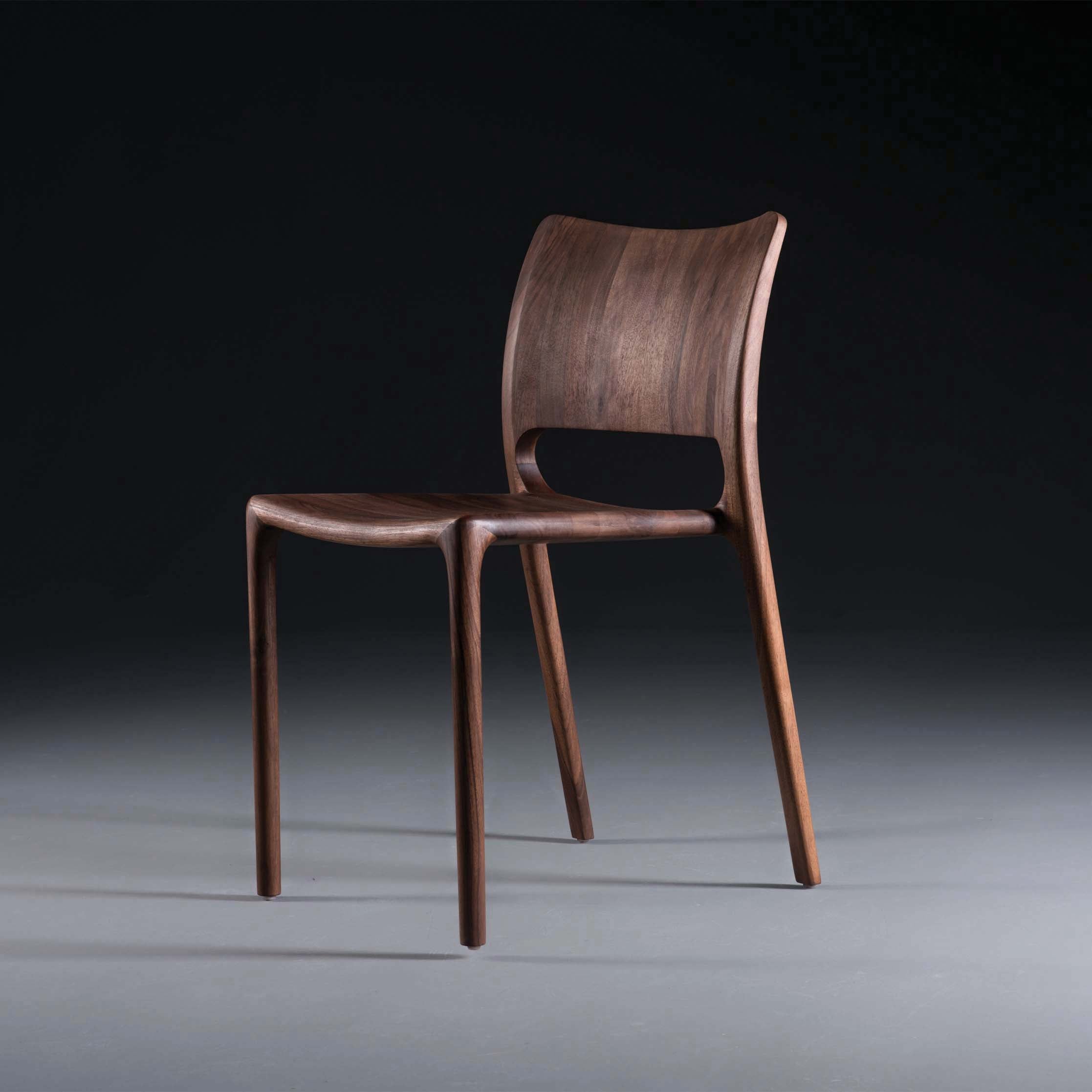 The Artisan LATUS Chair, crafted from solid wood and finished with natural oils for an elegant sheen, showcases minimalist design with its curved backrest and slender, tapered legs. Its sleek modern look contrasts beautifully against a gradient background.