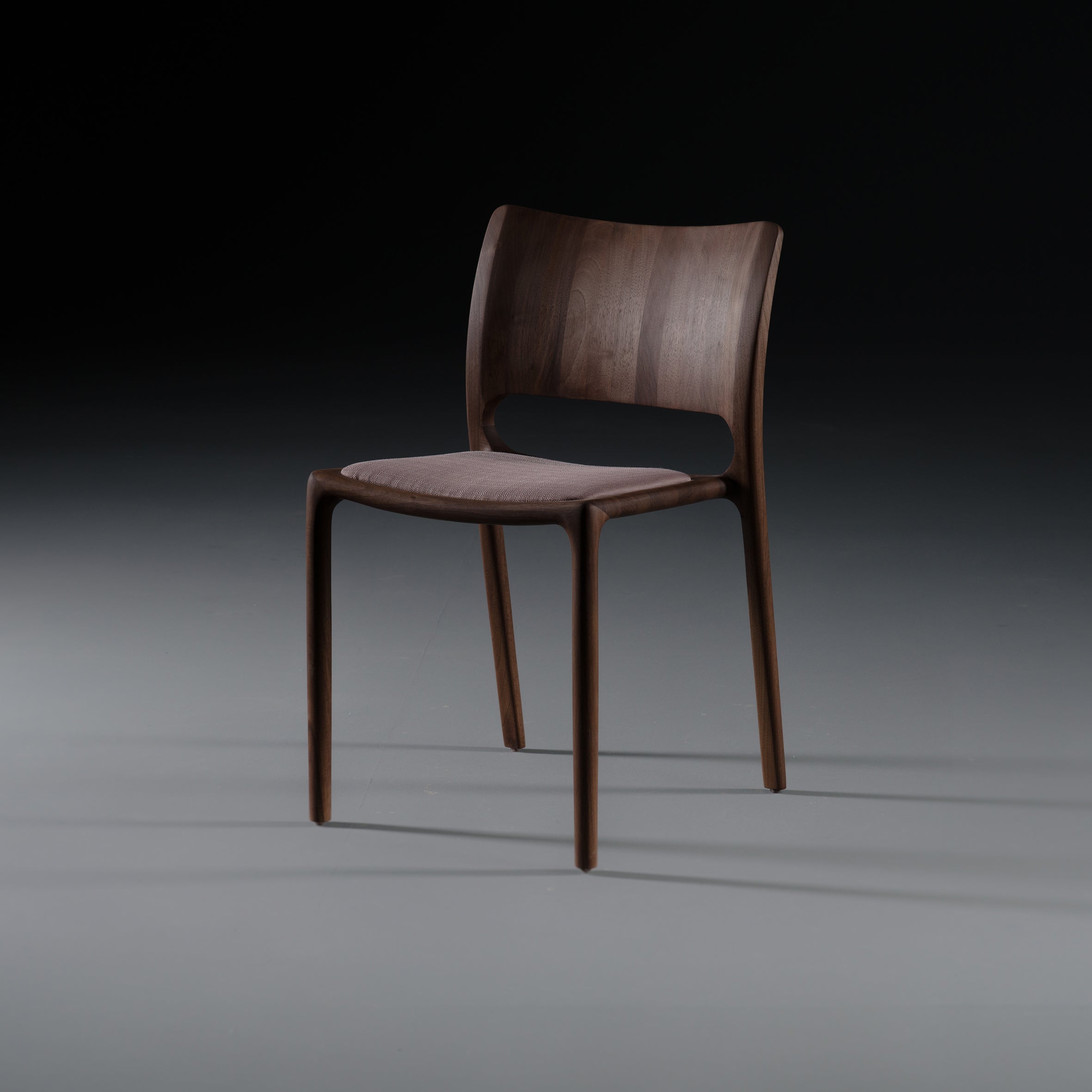 The LATUS Chair by Artisan is a modern, minimalist wooden chair featuring a curved backrest and cushioned seat, crafted from solid wood with natural oil finishing. Its smooth, dark finish highlights its sophisticated design against a gray gradient background.