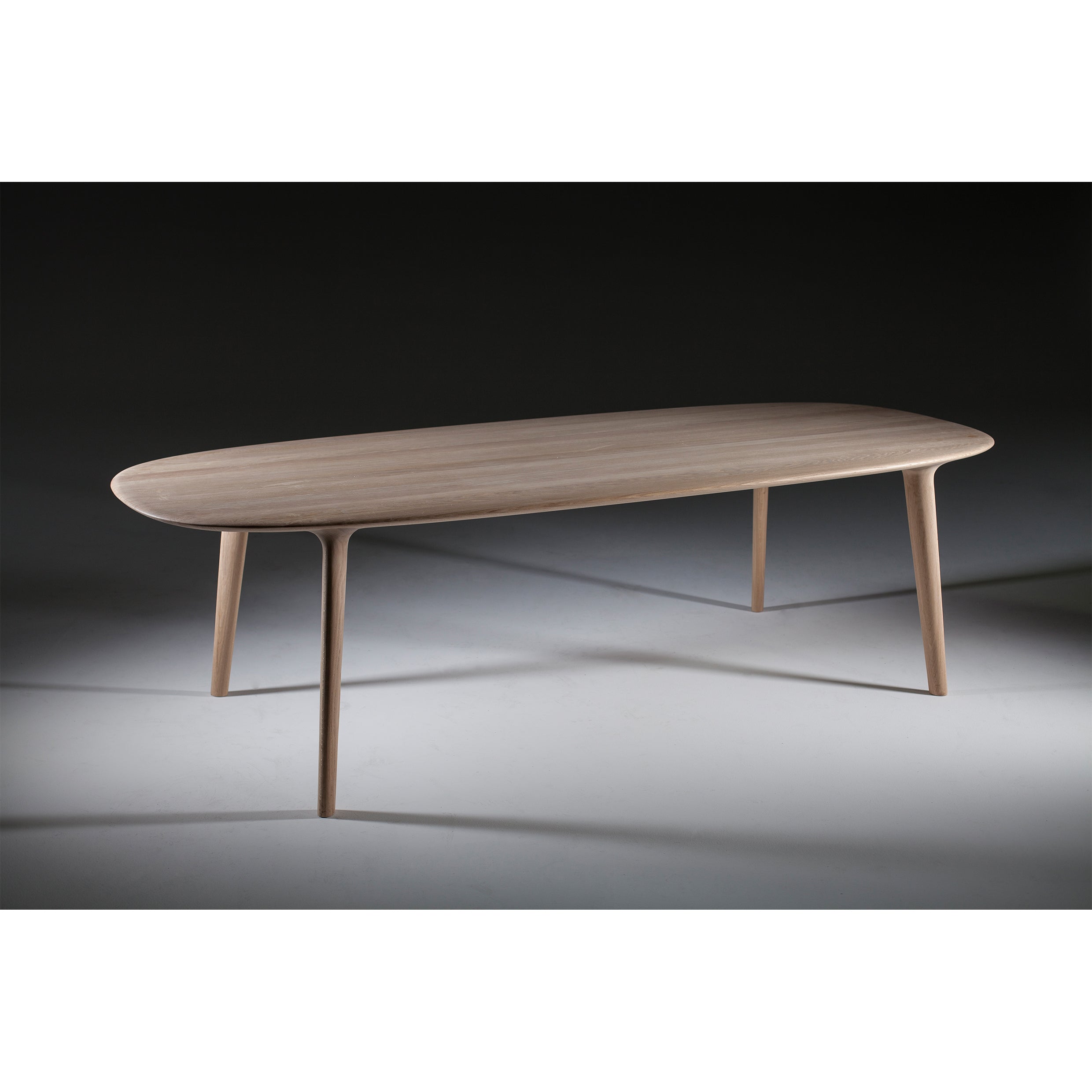 The LUC Table by Artisan, an oval-shaped coffee table made of light wood with slender, tapered legs, showcases exquisite craftsmanship against a dark background, creating a striking contrast.