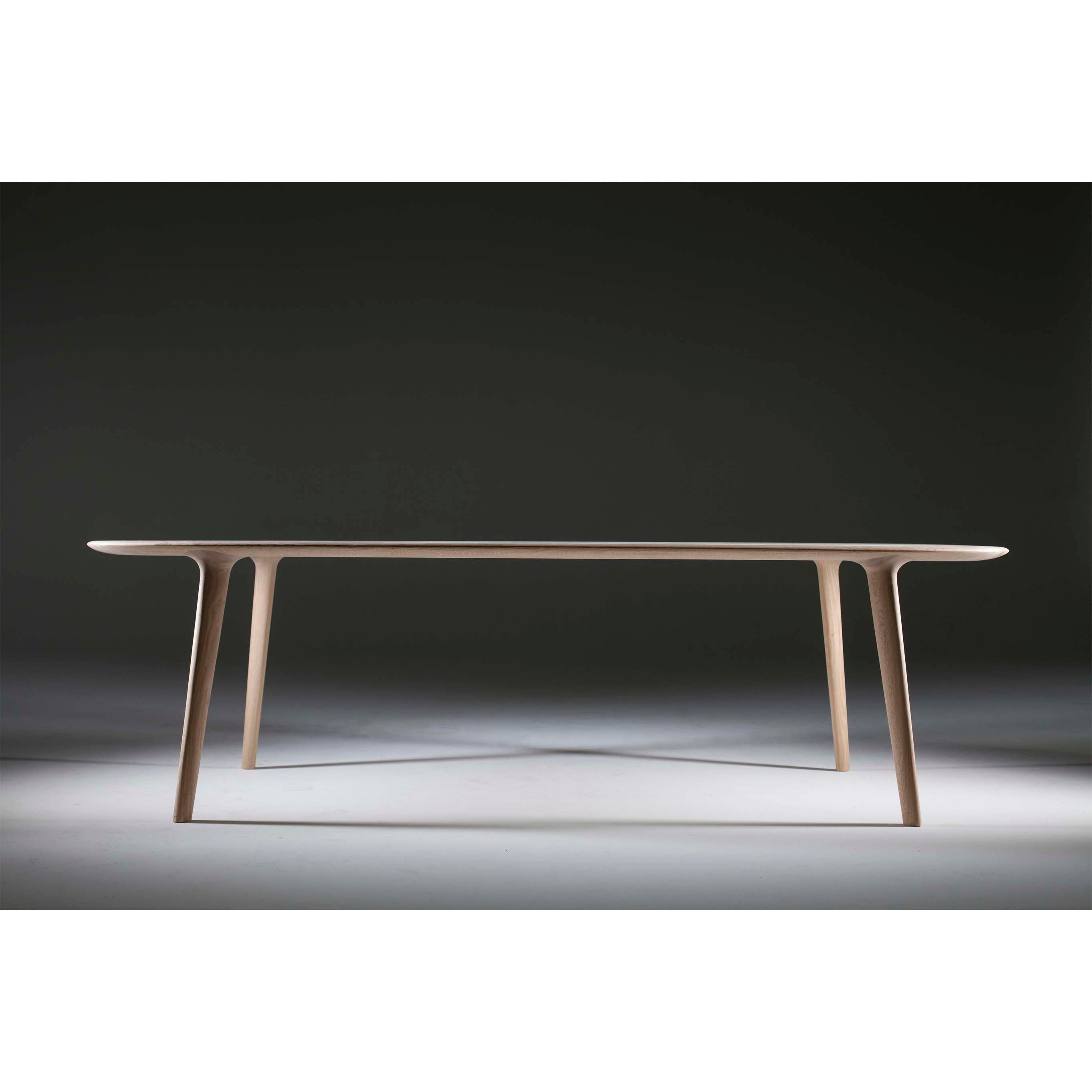 The LUC Table by Artisan embodies minimalist artisan craftsmanship with its sleek modern design, thin legs, and smooth flat surface. Photographed in a studio against a gradient dark background with soft lighting.