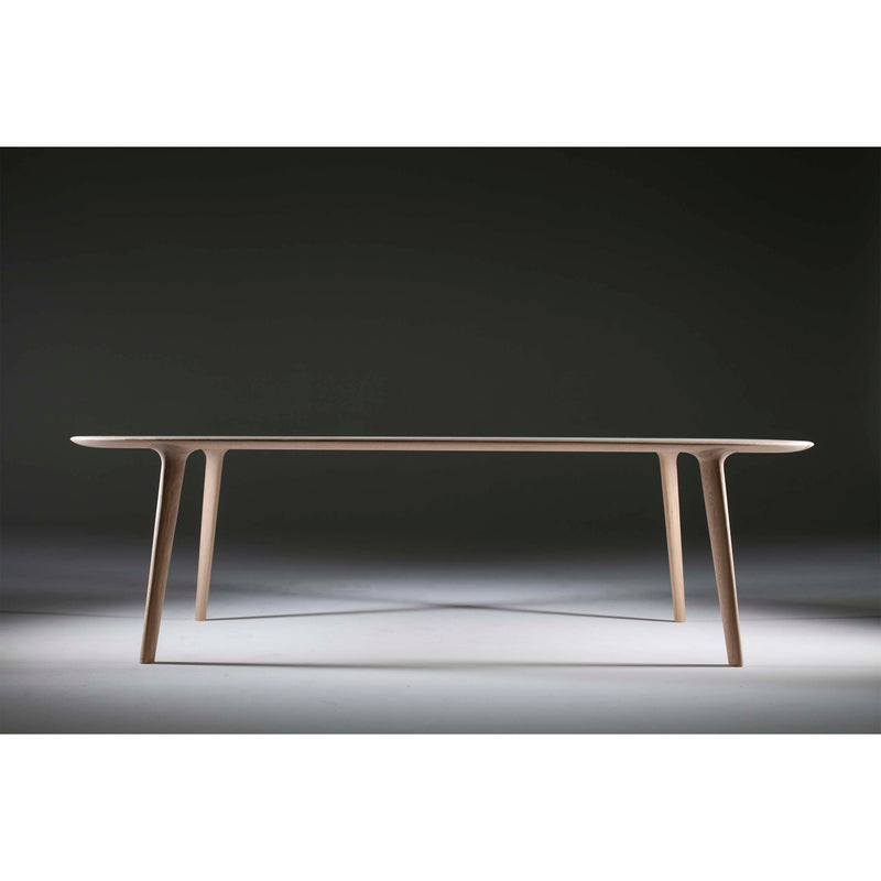 The LUC Table by Artisan embodies minimalist artisan craftsmanship with its sleek modern design, thin legs, and smooth flat surface. Photographed in a studio against a gradient dark background with soft lighting.