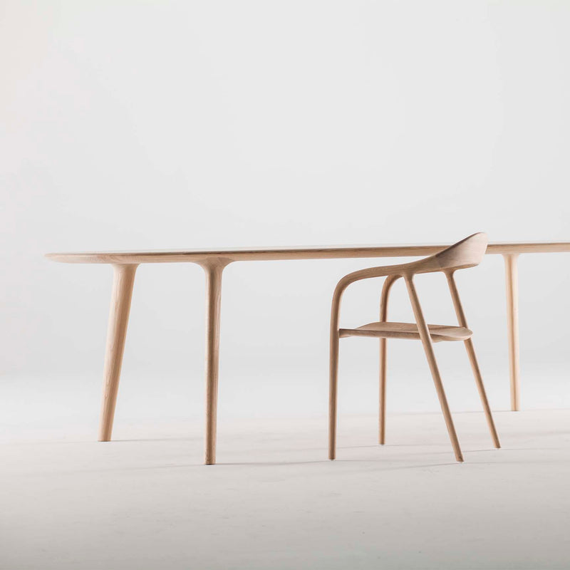 The Artisan LUC Table is a minimalist wooden table and chair set, showcasing artisan craftsmanship with sleek, curved legs and a simple design on a white background.