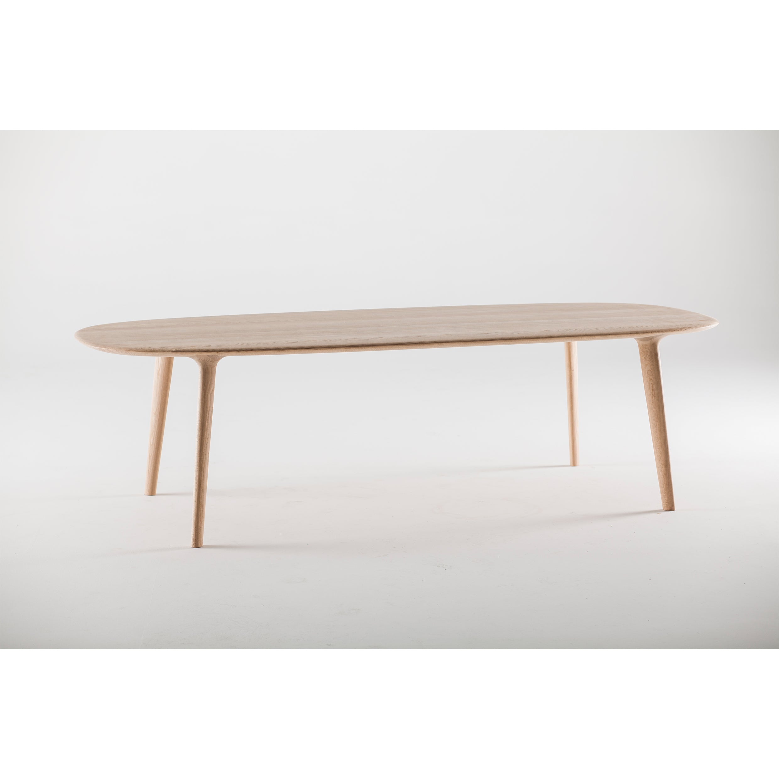 The LUC Table by Artisan is a minimalist piece with an oval top and four slender, tapered legs, showcasing artisan craftsmanship. Its light wood finish against a plain white background highlights its simple and modern design.