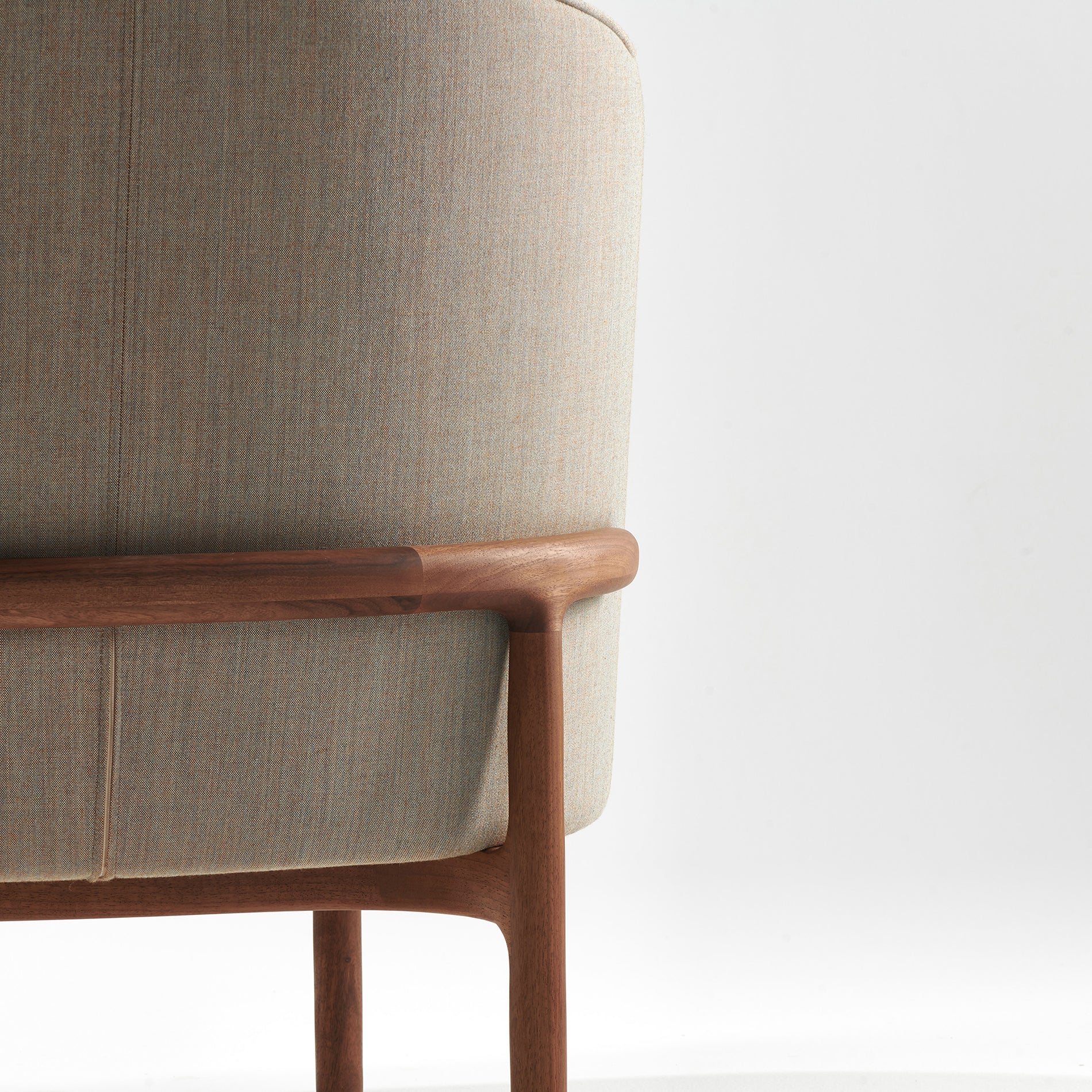 Close-up of Artisans MELA Lounge Chair Trimmed, featuring a light beige upholstered shell and smooth wooden frame. The chair embodies minimalist design with mid-century inspired elegance against a white background.