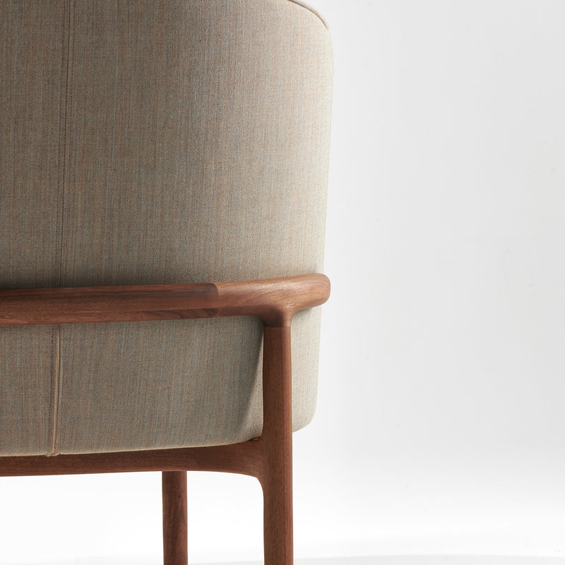 Close-up of Artisans MELA Lounge Chair Trimmed, featuring a light beige upholstered shell and smooth wooden frame. The chair embodies minimalist design with mid-century inspired elegance against a white background.