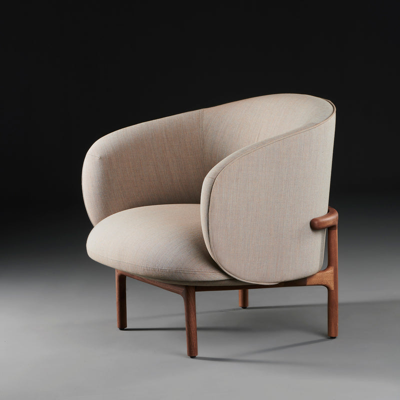 The MELA Lounge Chair Trimmed by Artisan, part of the Mela collection, features modern light beige upholstery and smooth rounded edges. Its sleek wooden frame and legs against a dark gradient backdrop showcase minimalist elegance with mid-century inspired aesthetics.