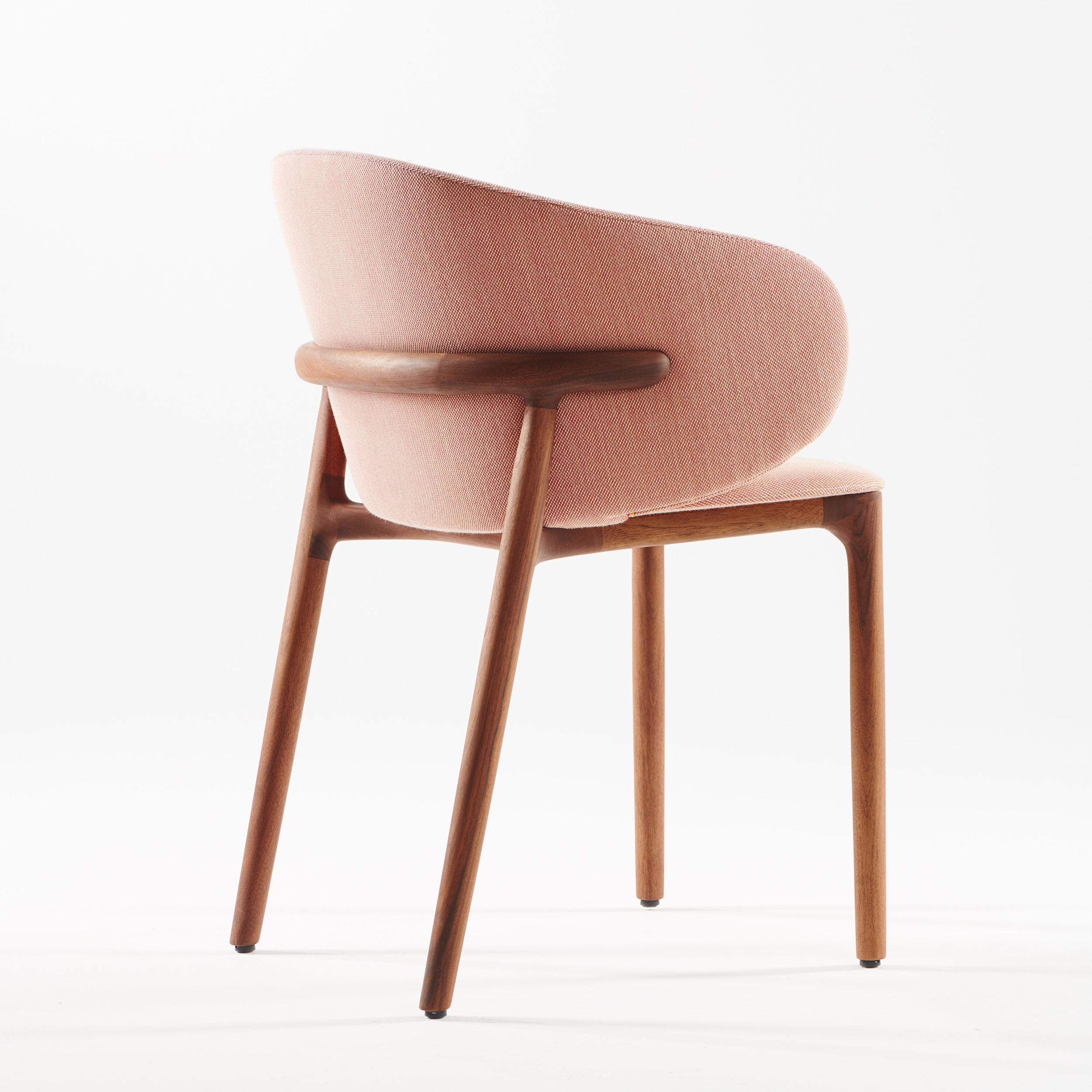 The Artisan Mela Chair features a pink upholstered curved backrest and sturdy wooden structure. Its elegant, clean lines beautifully merge contemporary and mid-century-inspired styles, all set against a plain white background.