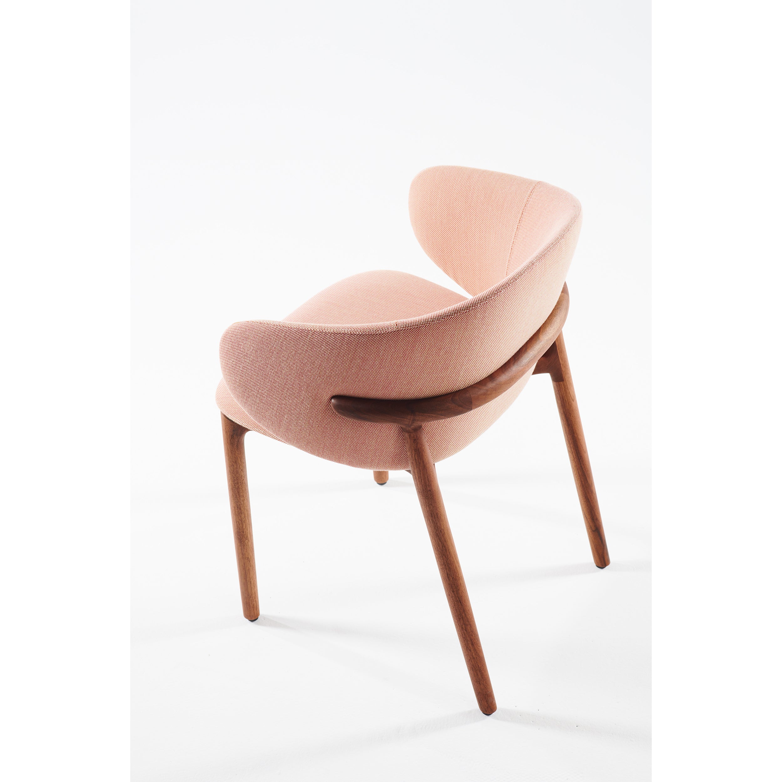 Introducing the Artisan Mela Chair, a modern seating solution with light pink upholstery and smooth, rounded wooden legs. It features a curved upholstered backrest and a wooden handlebar, blending mid-century charm with contemporary style.