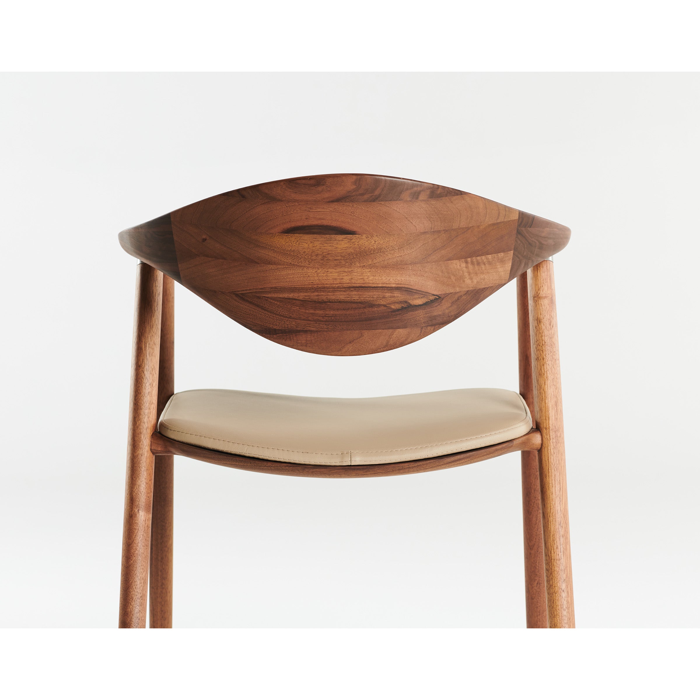 The NARU Chair by Artisan features a minimalist design with a curved backrest and light-colored cushioned seat. Crafted from solid wood, it showcases smooth lines and a natural finish enhanced by eco-friendly oils, set against a white background.