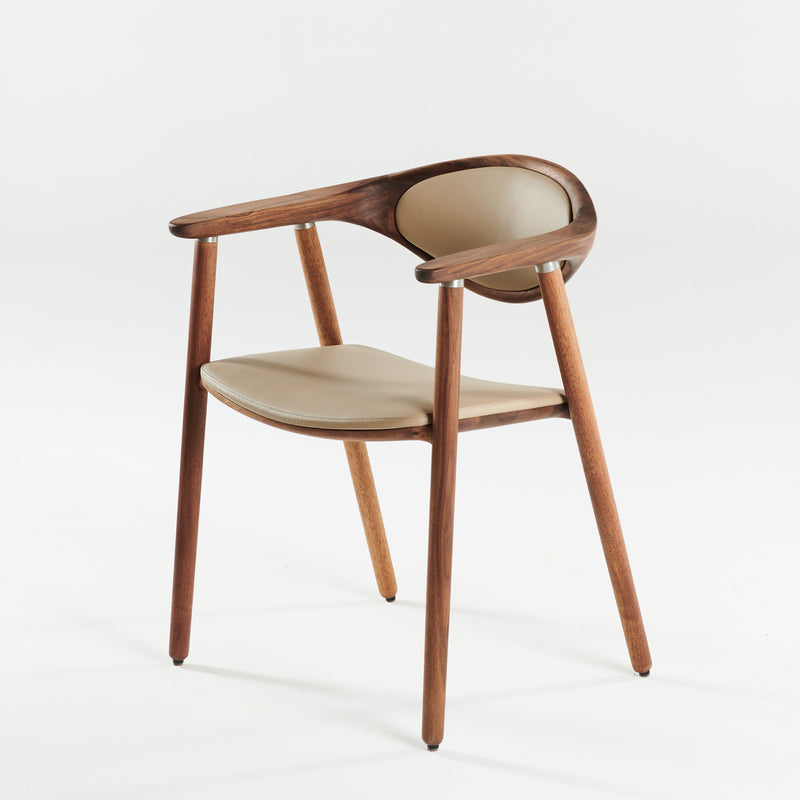 The Artisan NARU Chair features a modern design with solid wood, natural oil finish, curved backrest, and armrests. It includes light tan cushions on the seat and back and stands on four tapered legs against a plain white background.