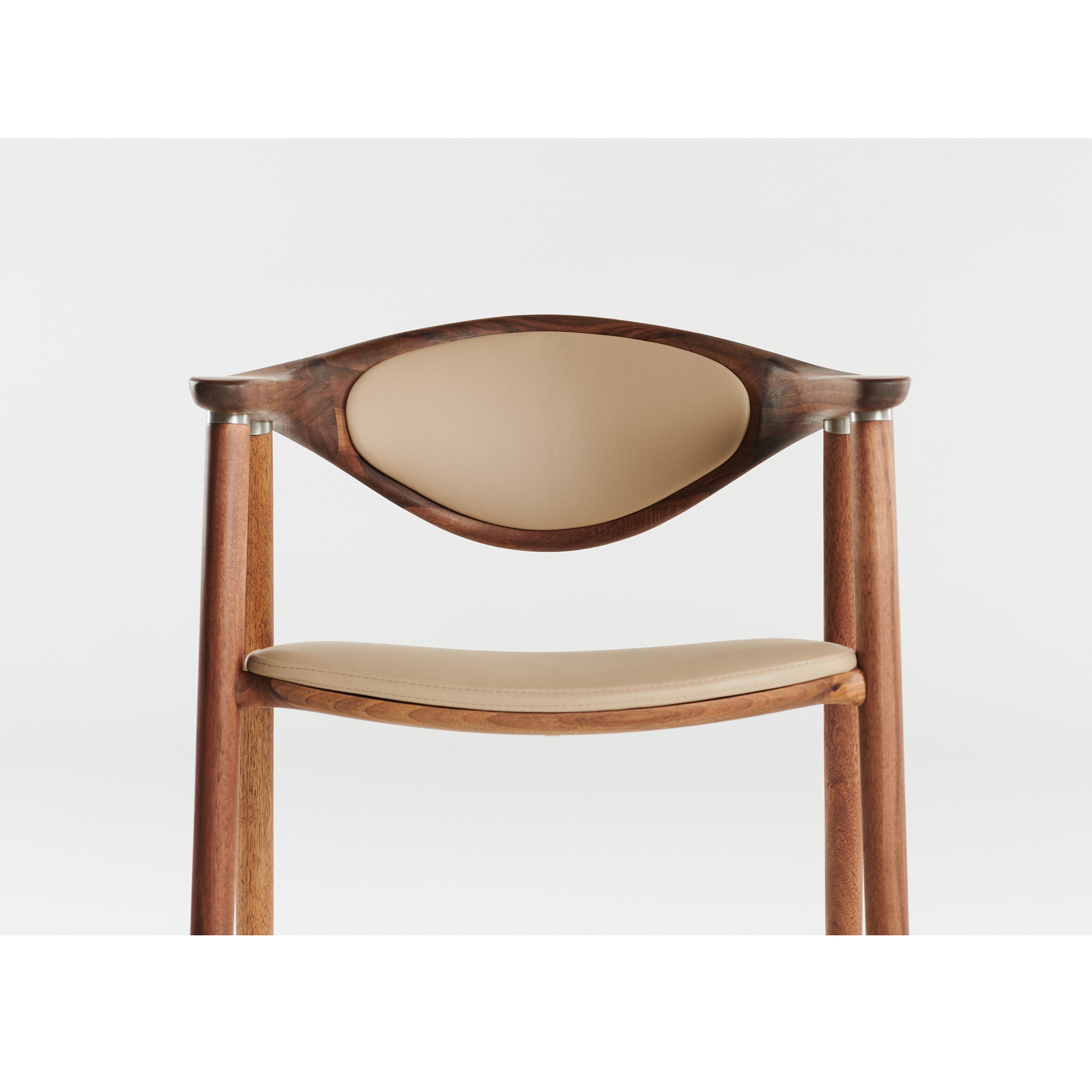 The Artisan NARU Chair features a minimalist design with a curved backrest and a seat upholstered in light beige leather. Crafted from solid wood polished with natural oils, it showcases modern elegance against a plain background while being environmentally friendly.