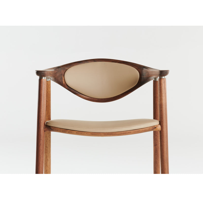 The Artisan NARU Chair features a minimalist design with a curved backrest and a seat upholstered in light beige leather. Crafted from solid wood polished with natural oils, it showcases modern elegance against a plain background while being environmentally friendly.