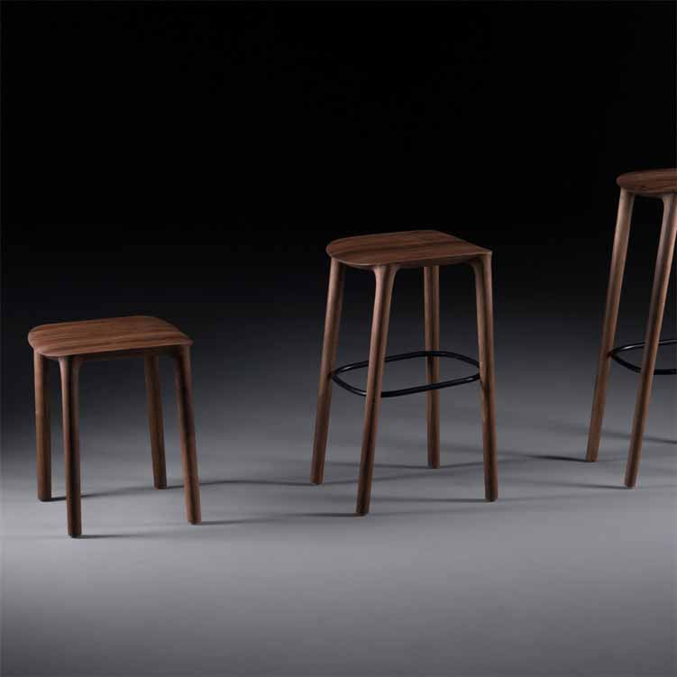 Three NEVA Stools from Artisan, each with a rectangular seat and craftsmanship featuring four legs, sit on a smooth, dark surface. Their varying heights create an elegant display against the black background.