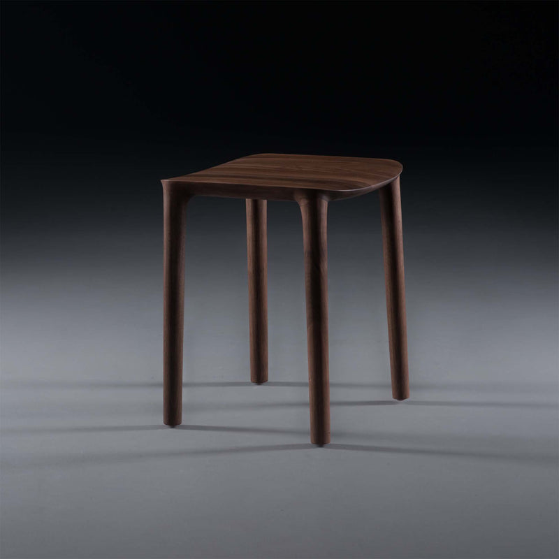 The NEVA Stool by Artisan is a minimalist design featuring four slender legs and a smooth, slightly curved seat, set against a dark gradient background.