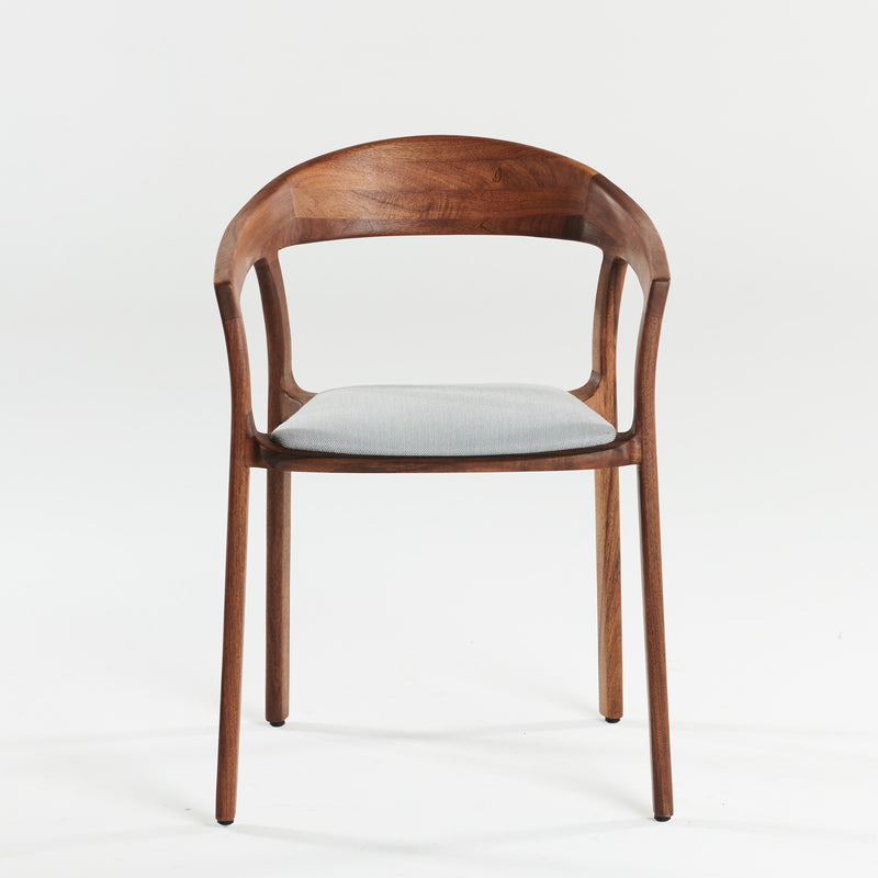 The TARA Armchair by Artisan is a wooden chair with a solid wood build, curved backrest, and open design. It features a light gray cushioned seat on a minimalist frame, crafted from eco-friendly materials and finished with natural oils, standing elegantly against a plain white background.