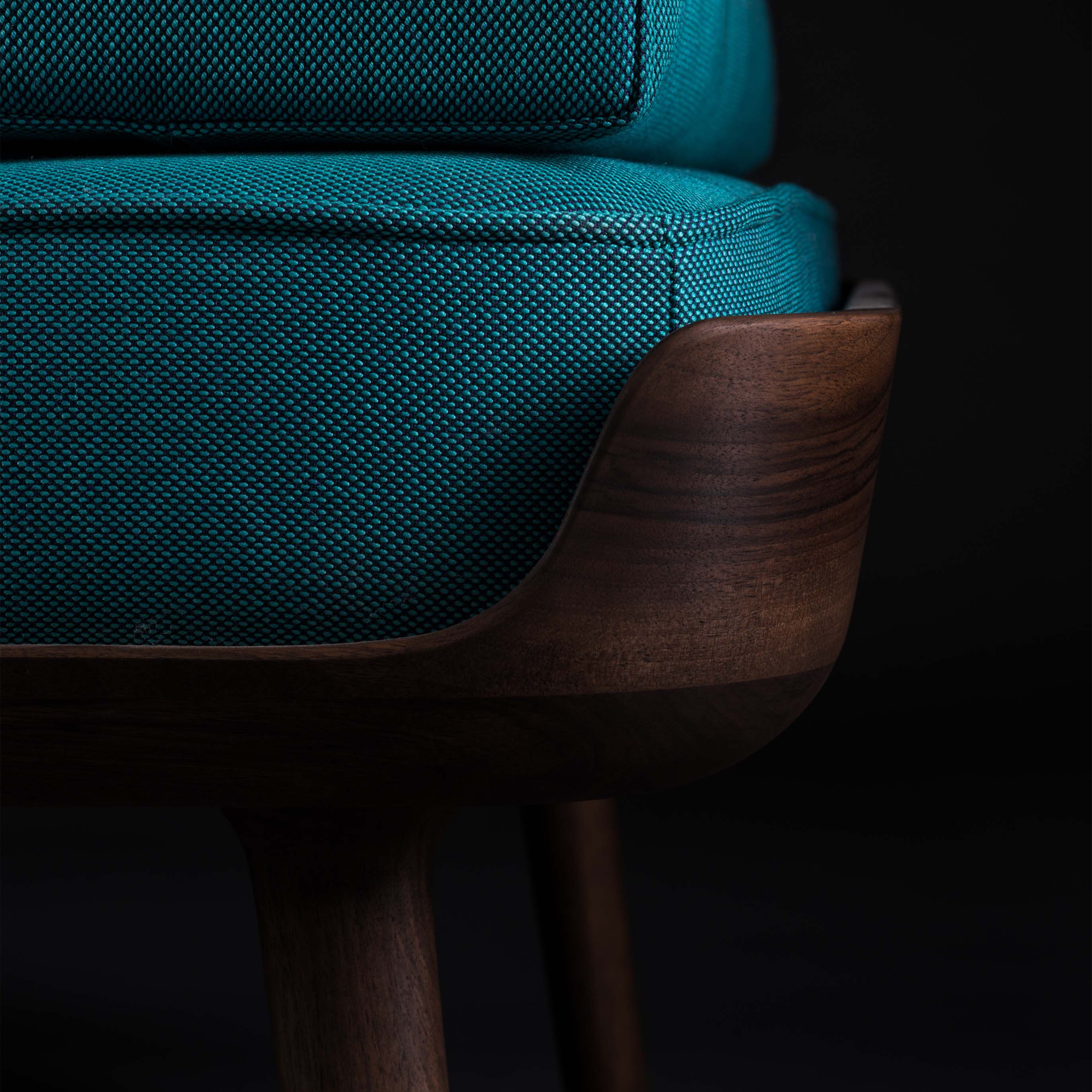 Close-up of the THOR Daybed by Artisan featuring teal upholstery and a dark wooden frame, highlighting the natural wood texture and smooth finish. A black background emphasizes its elegant design crafted from eco-friendly materials.