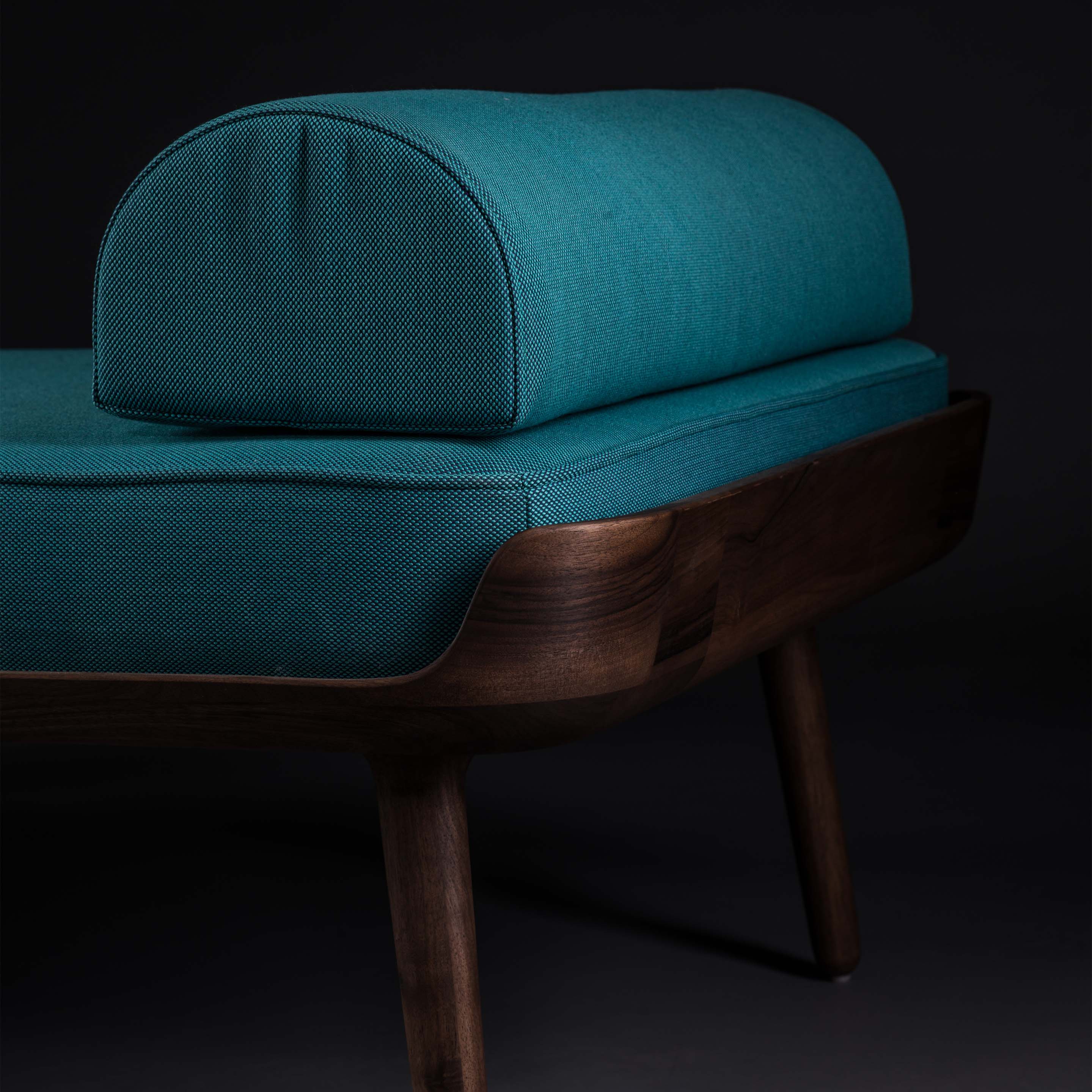 The THOR Daybed by Artisan features a sleek, minimalist design with a dark wood frame, teal cushions, and tapered legs. Crafted from eco-friendly materials, its style emphasizes the natural wood texture against a dark background.