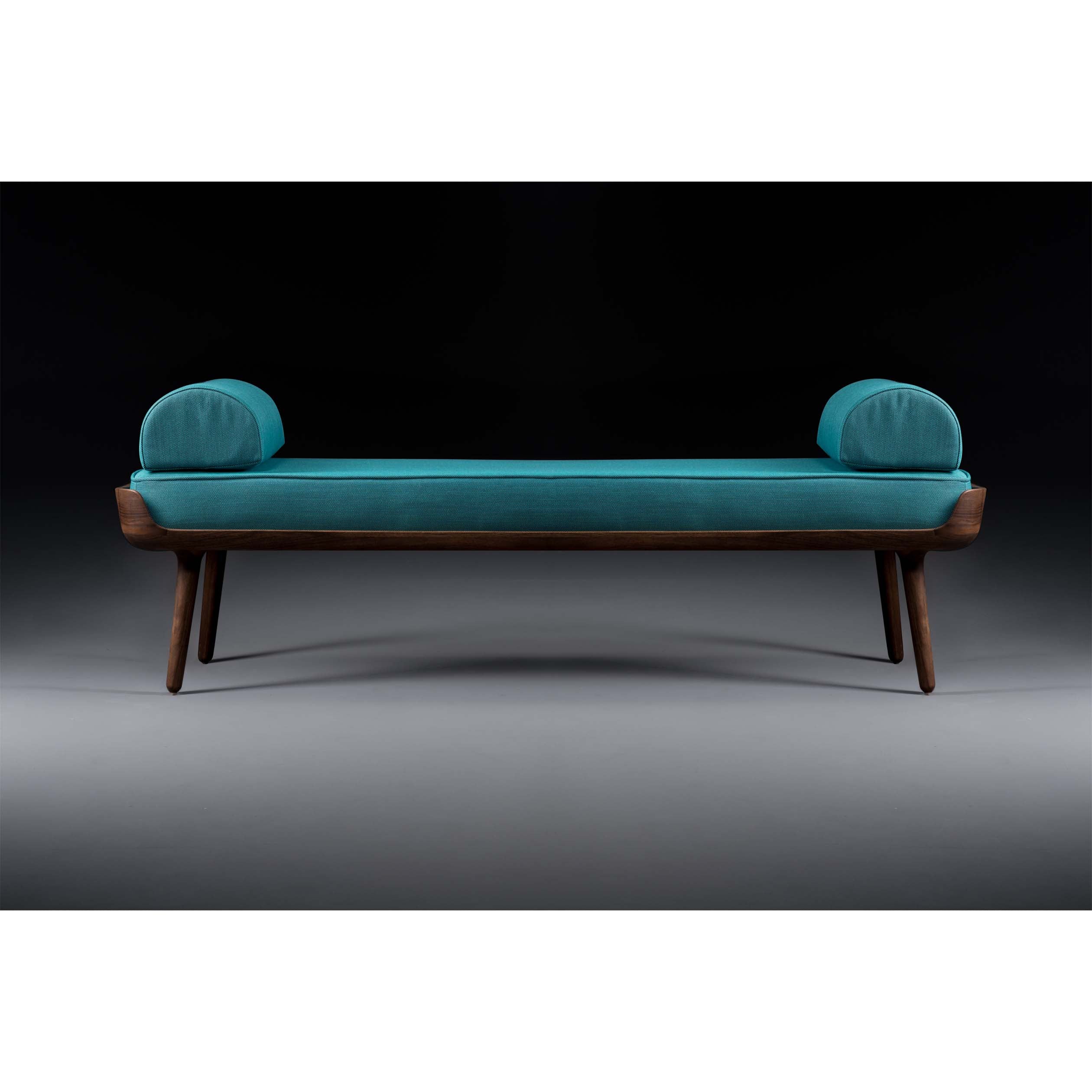 The THOR Daybed by Artisan features a sleek, modern design with solid wood construction and teal cushioning. Its cylindrical armrests, natural wood texture, and dark frame highlight its minimalist style and environmentally-friendly materials.