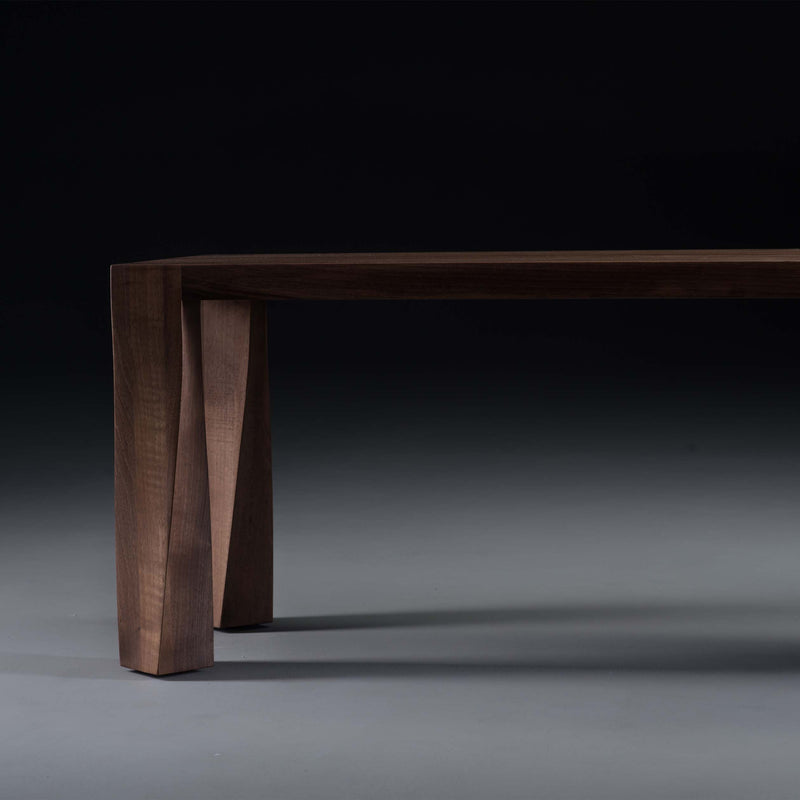 Close-up of the TOR Bench by Artisan, featuring a dark wooden tabletop and distinctive angled legs against a dark background. Crafted from solid wood and treated with natural oils, it highlights the wood grain for an eco-friendly, minimalist, modern look.