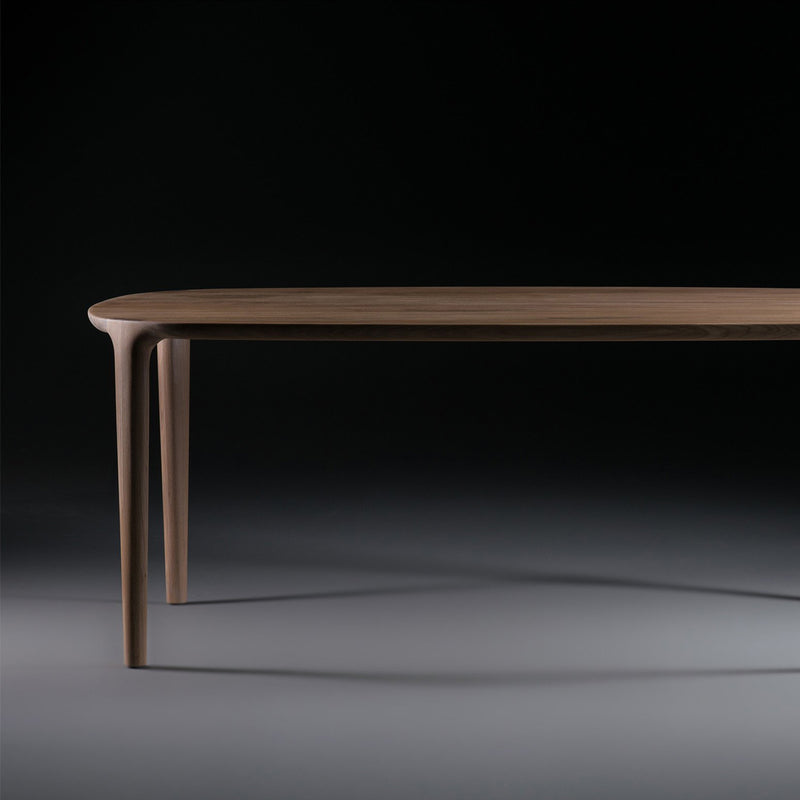 The Artisan WU Table, crafted from solid wood, features elegantly tapered legs. Set against a dark background, lighting highlights its luxurious texture and smooth surface, showcasing its minimalist design.