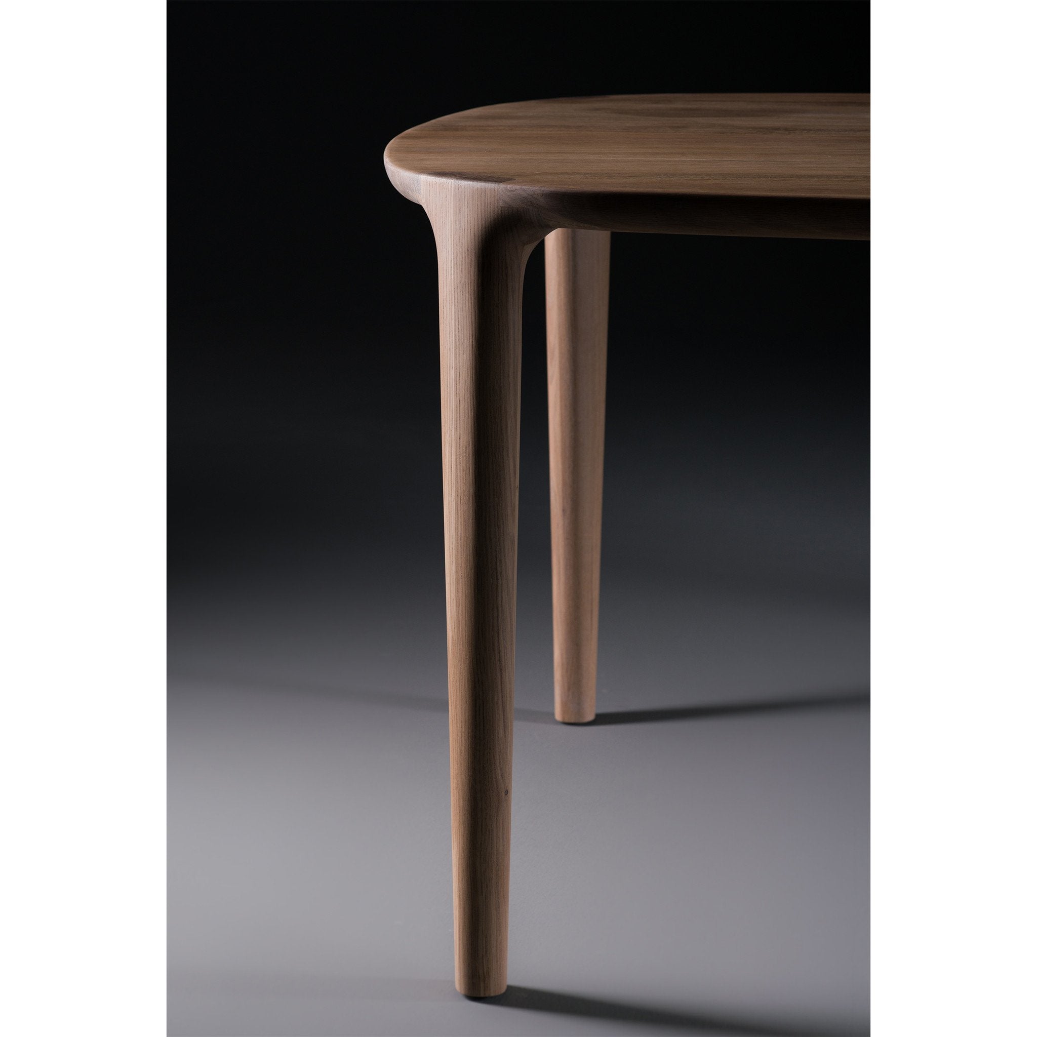The WU Table by Artisan showcases smooth craftsmanship and elegant design with sleek, rounded legs and luxurious wood texture, beautifully highlighted against a dark background.