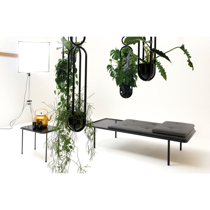 2PM Day & Night Daybed shown with black metal frame and gray cushions, surrounded by hanging plants in modern setting