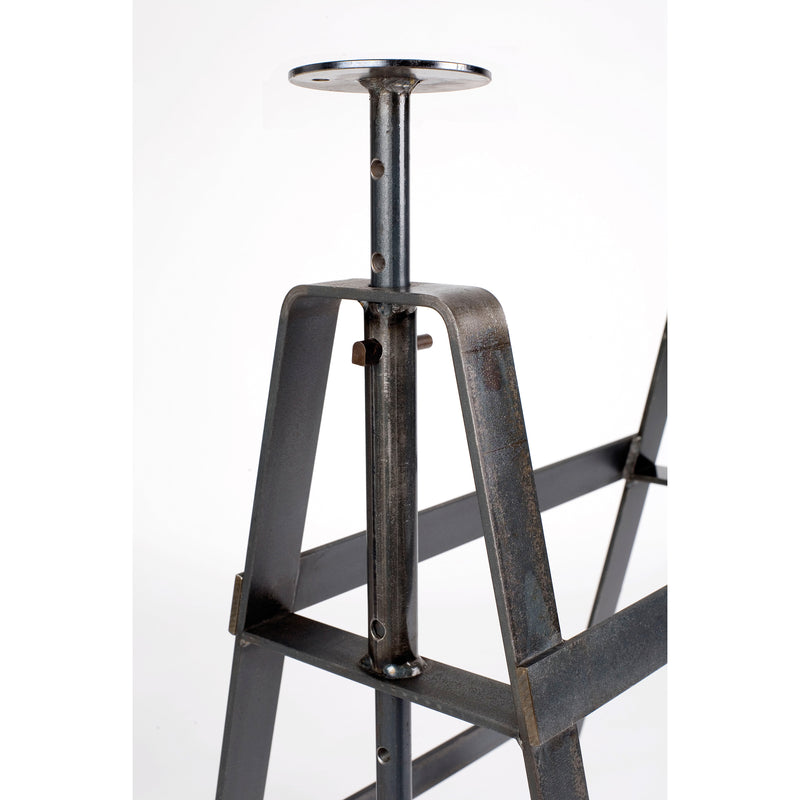 Close-up of the Affe Trestle by Atelier Haussmann, an industrial-style, height-adjustable table base in thick, dark oiled raw steel with visible screws and a vertical adjustment mechanism, topped with a round plate. The plain white background highlights its rugged elegance.