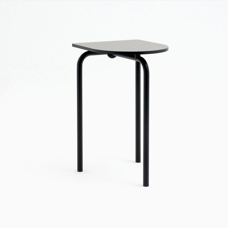 Meet the Piombino Alto 700 by Atelier Haussmann: a minimalist black side table featuring three curved metal legs and a semi-circular top. Its sleek, modern design draws from industrial aesthetics, standing gracefully against a plain white backdrop.
