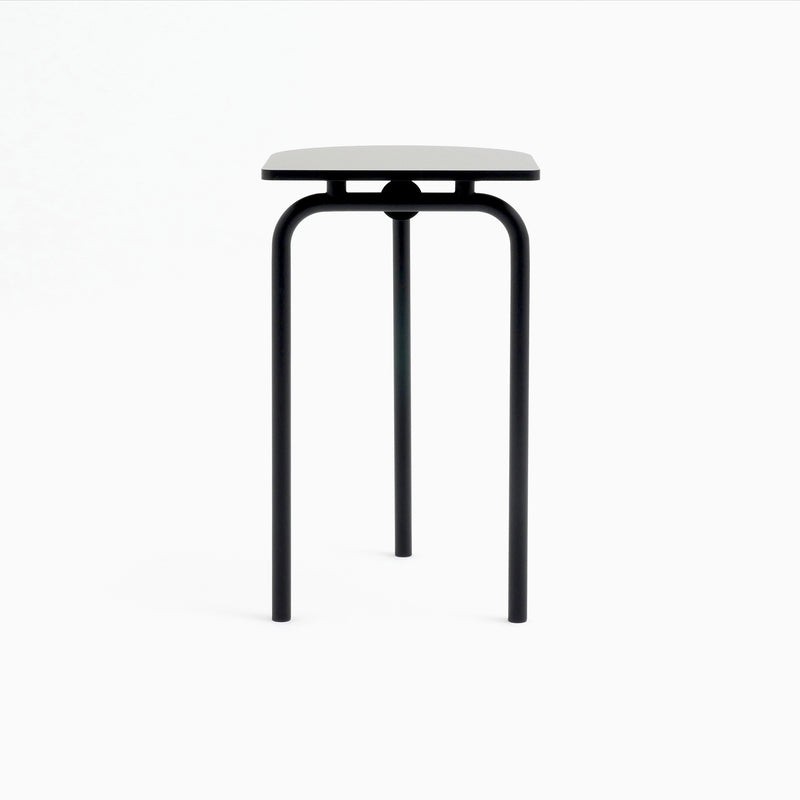 The Piombino Alto 700 by Atelier Haussmann is a minimalist stool featuring a square white seat and three black metal legs, showcasing an industrial design against a plain white background.