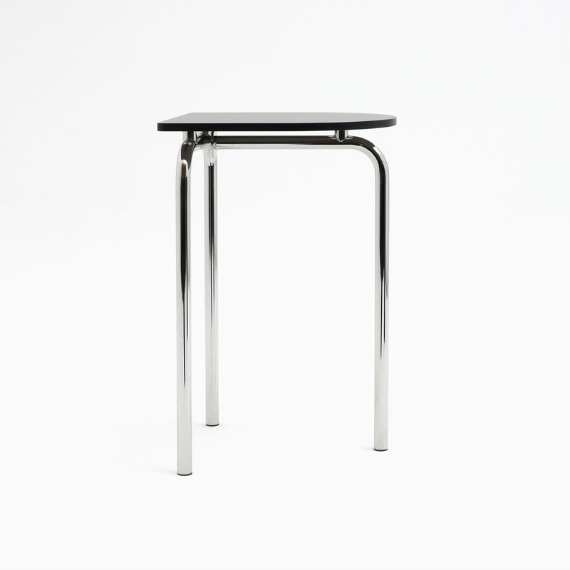 The Piombino Alto 700 by Atelier Haussmann is a minimalist table with a black triangular top and three polished chrome legs, exuding an industrial and modern aesthetic that complements any modular system.