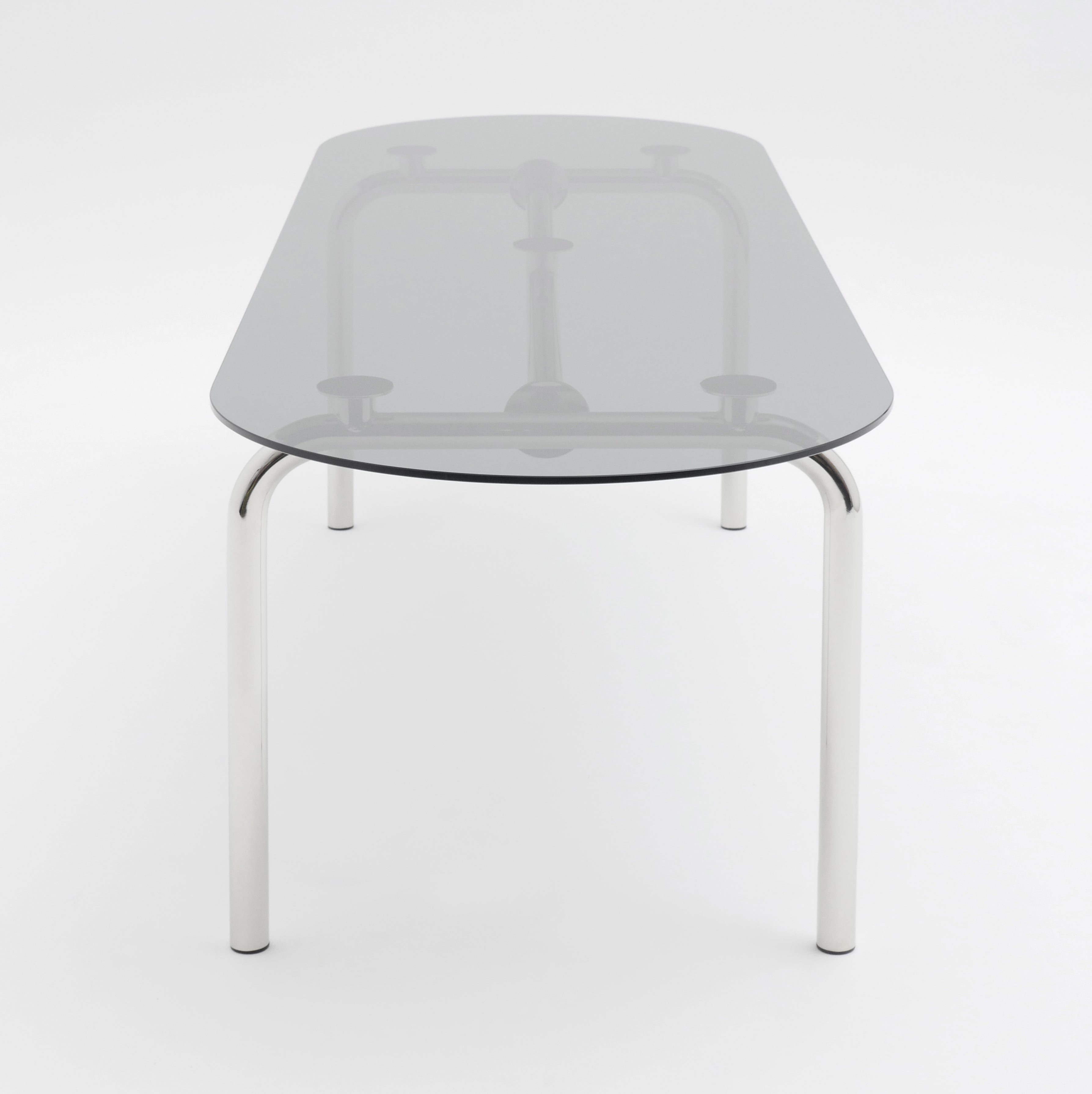 The Piombino Basso Table by Atelier Haussmann boasts a reflective glass top supported by four shiny steel tube legs, elegantly centered against a plain white background to highlight its sleek design and modular system versatility.
