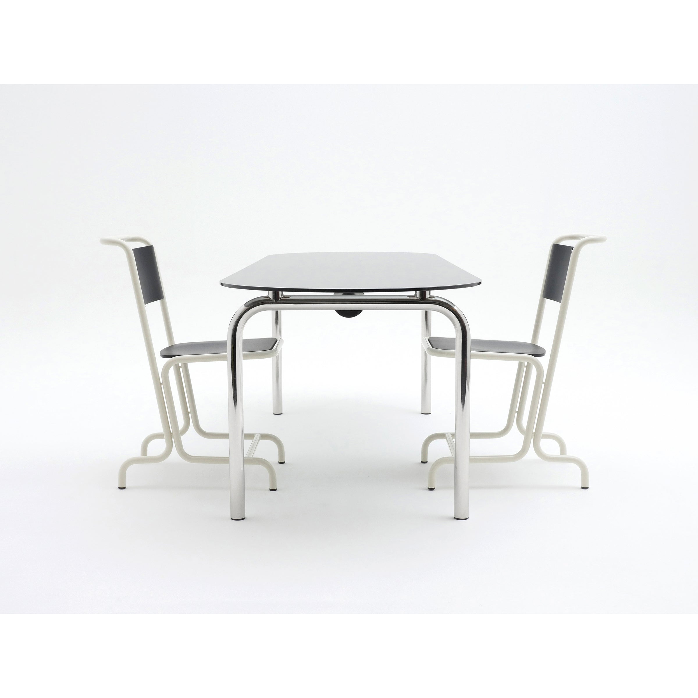 A minimalist setting highlights an Atelier Haussmann Piombino Basso Table featuring sleek metal frames, accompanied by two black and white chairs. The modular design showcases dark surfaces against a plain white background, embodying modern industrial style with steel tube construction.