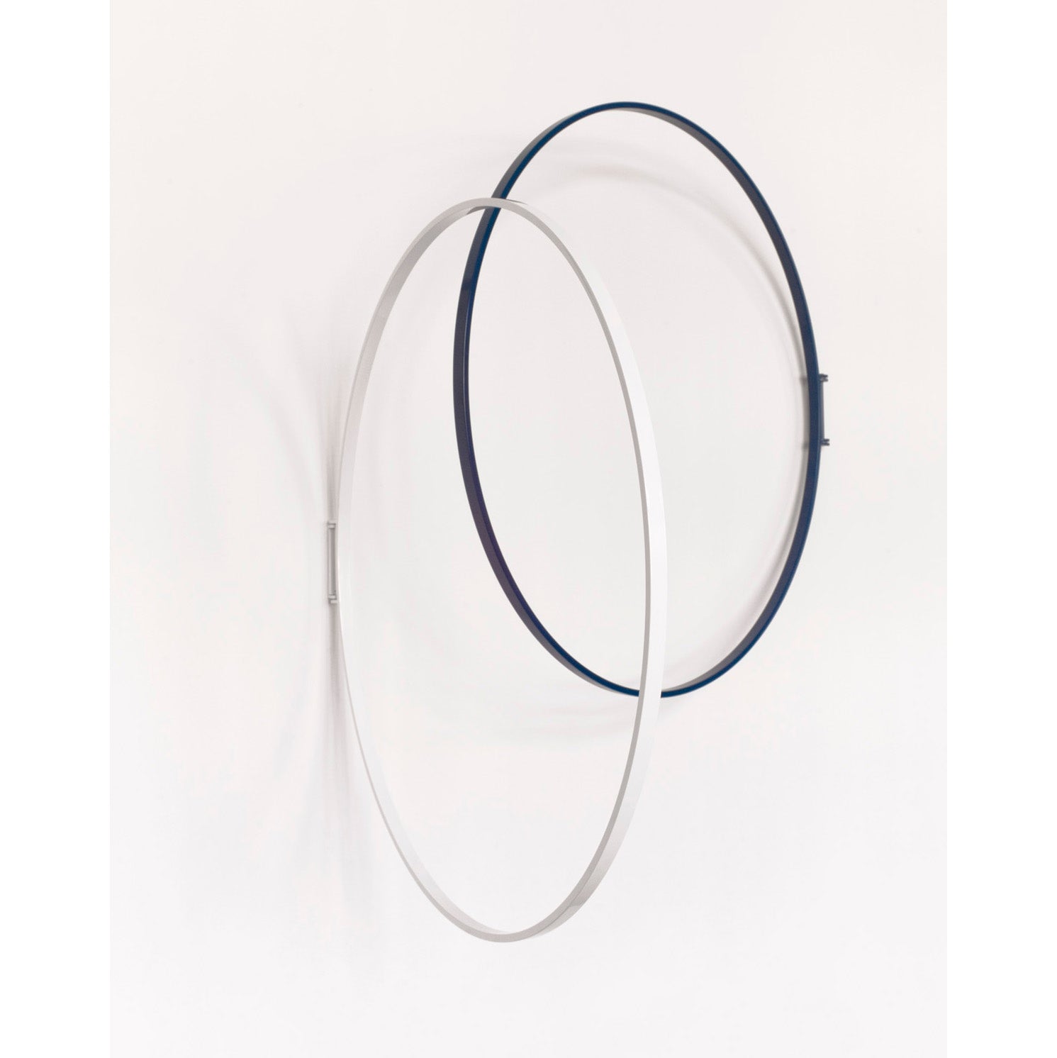The minimalist three-dimensional geometric design by Atelier Haussmann features two intersecting rings, one silver and the other dark blue, mounted on a white wall. This Rings decorative object adds a modern touch to any space.