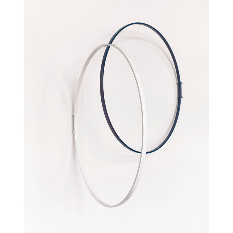 The minimalist three-dimensional geometric design by Atelier Haussmann features two intersecting rings, one silver and the other dark blue, mounted on a white wall. This Rings decorative object adds a modern touch to any space.