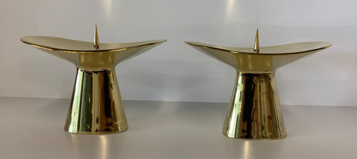 Two gold Candlestick #3469 from Werkstätte Carl Auböck, with pointed tops and a polished finish, rest on a white surface against a neutral backdrop, reflecting light beautifully.
