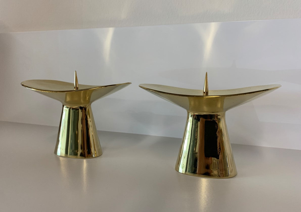 Two modern, gold-toned Candlestick #3469 from Werkstätte Carl Auböck sit side by side on a white surface, each featuring a sleek, flared design and a central spike for candle securing.
