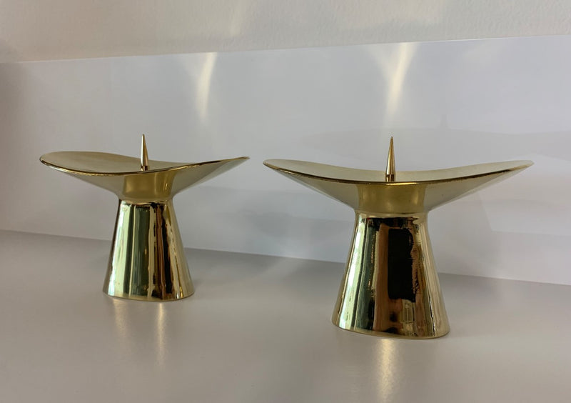 Two modern, gold-toned Candlestick #3469 from Werkstätte Carl Auböck sit side by side on a white surface, each featuring a sleek, flared design and a central spike for candle securing.