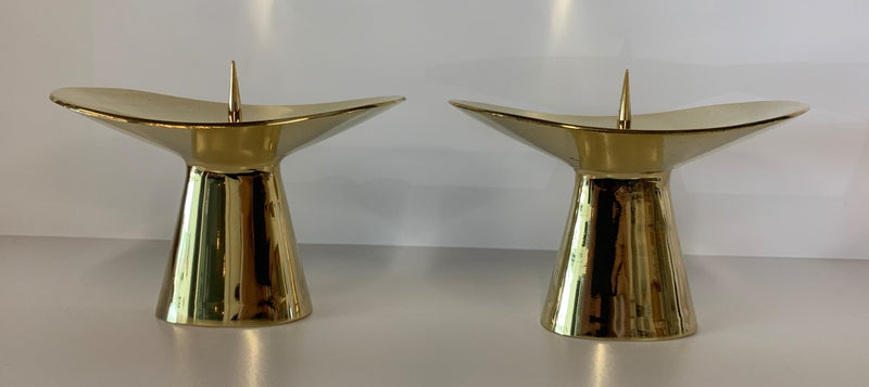Two gold Candlestick #3469 from Werkstätte Carl Auböck, with pointed tops and a polished finish, rest on a white surface against a neutral backdrop, reflecting light beautifully.
