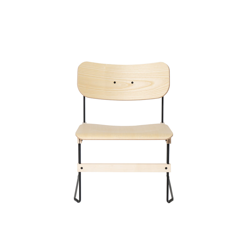 Front view of Moormann’s Brutissimo: a minimalist wooden lounge chair featuring a light molded wood seat and backrest, supported by slender black metal legs, showcasing a simple and modern design.
