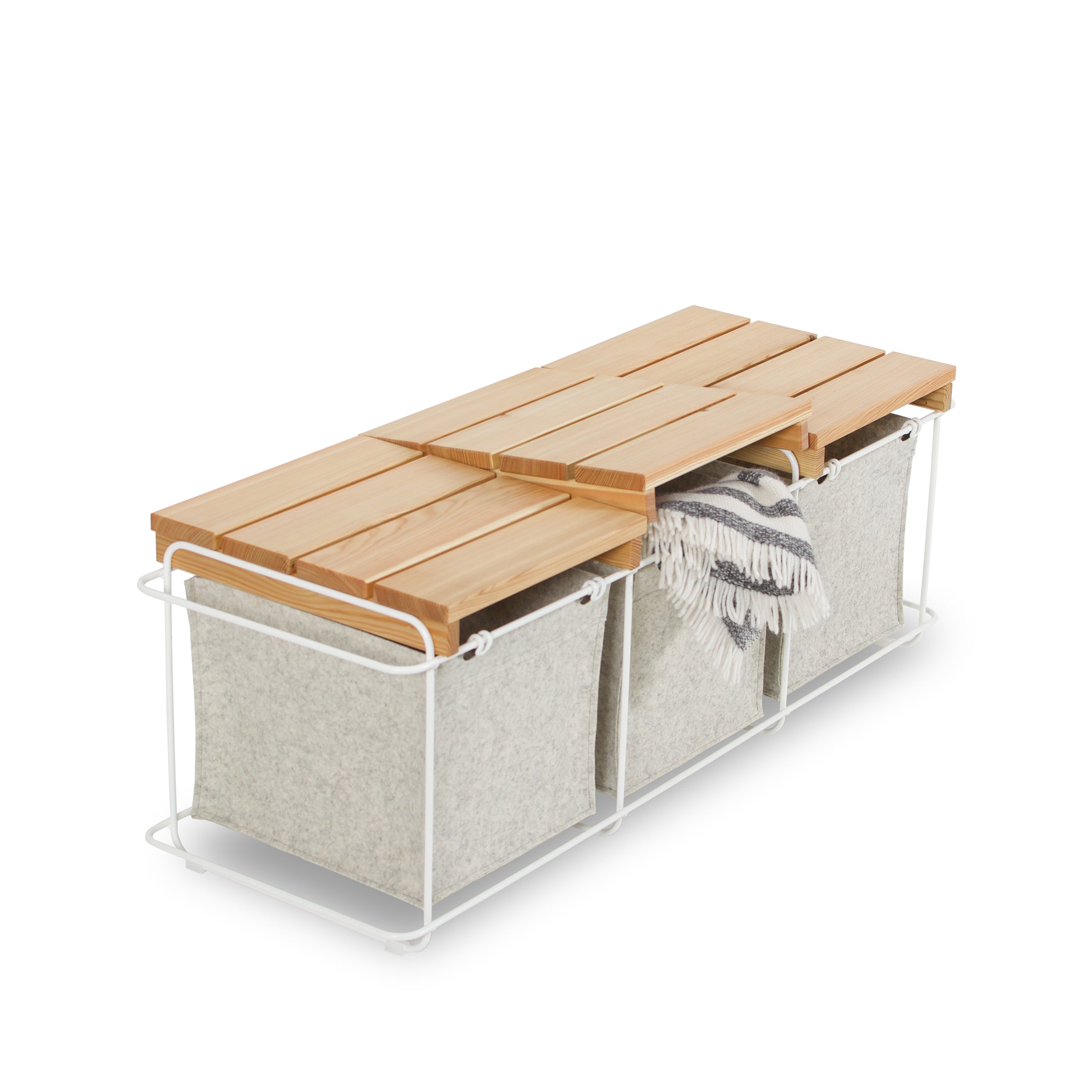 Bartmann Berlins Grit Indoor bench features a slatted wooden top with storage compartments. It has a white powder-coated stainless steel frame, two wool felt bins, and a striped blanket corner visible, blending functionality with charm.