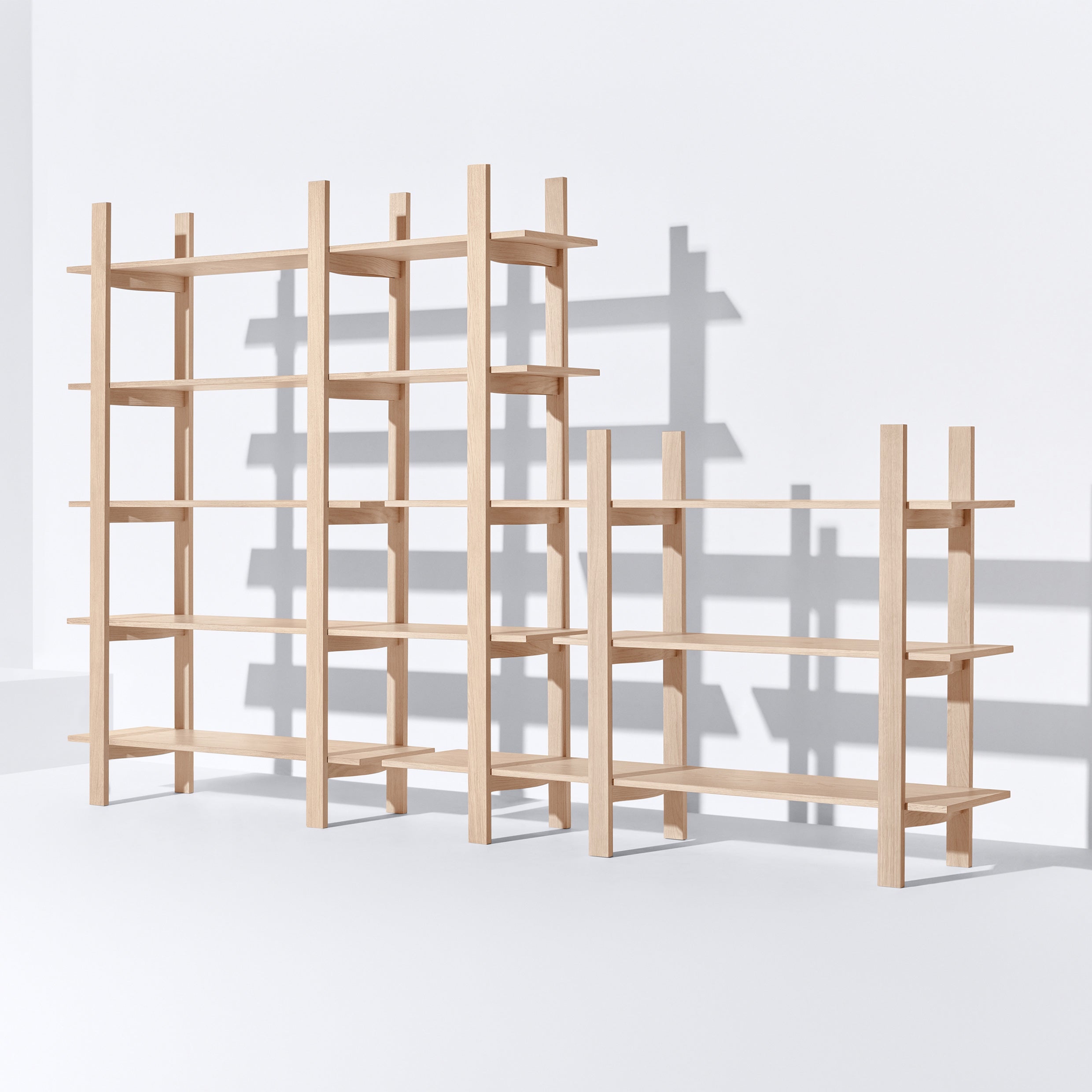 Against a light background, two minimalist Tonus shelves from Bartmann Berlin stand tall. These freestanding wooden units each feature five levels with both vertical and horizontal supports, creating subtle shadows on the surface behind them.