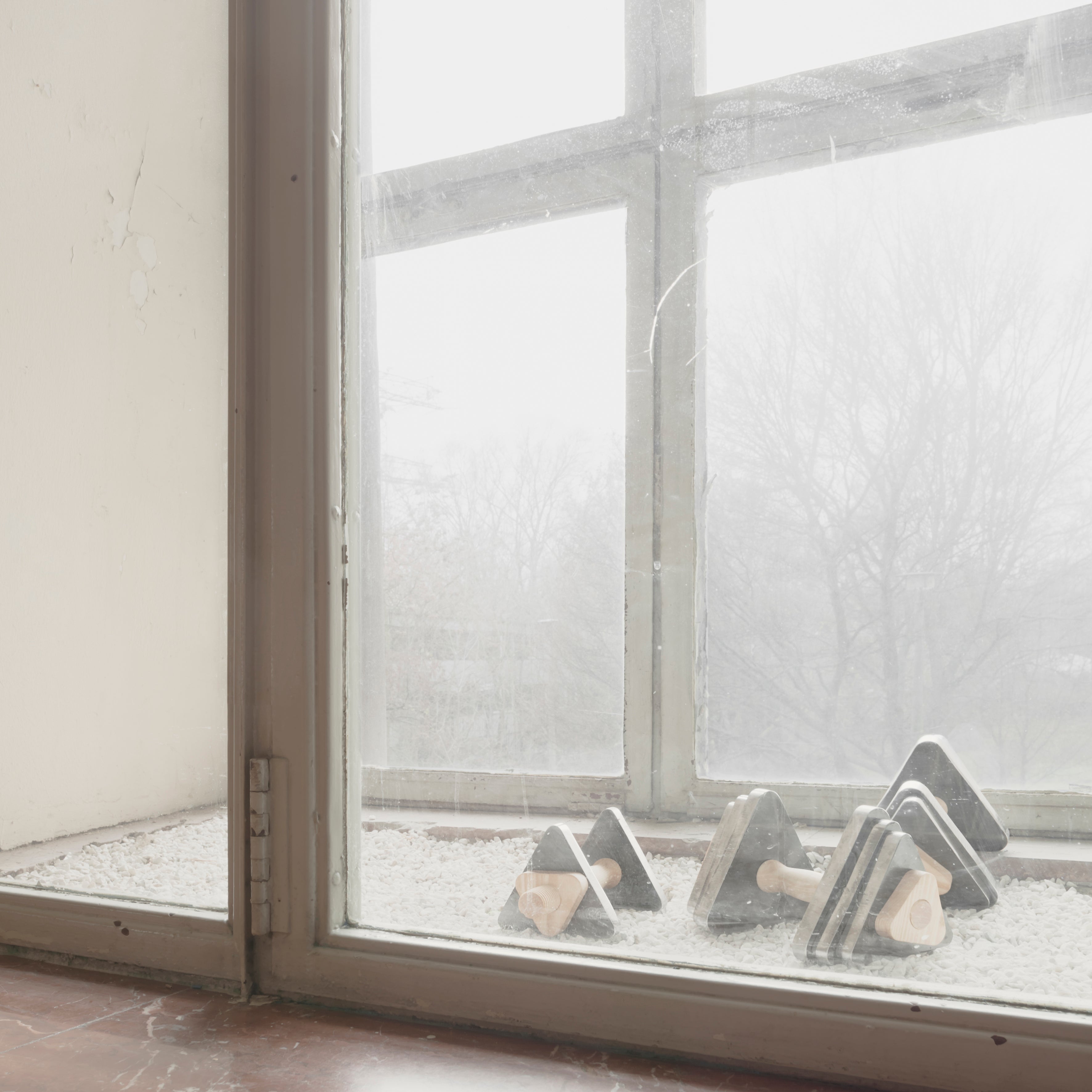 Trimm Dich dumbbells by Bartmann Berlin sit on a maple wood window sill overlooking a misty window, with an overcast sky beyond. The minimalist scene creates a calm, quiet atmosphere.