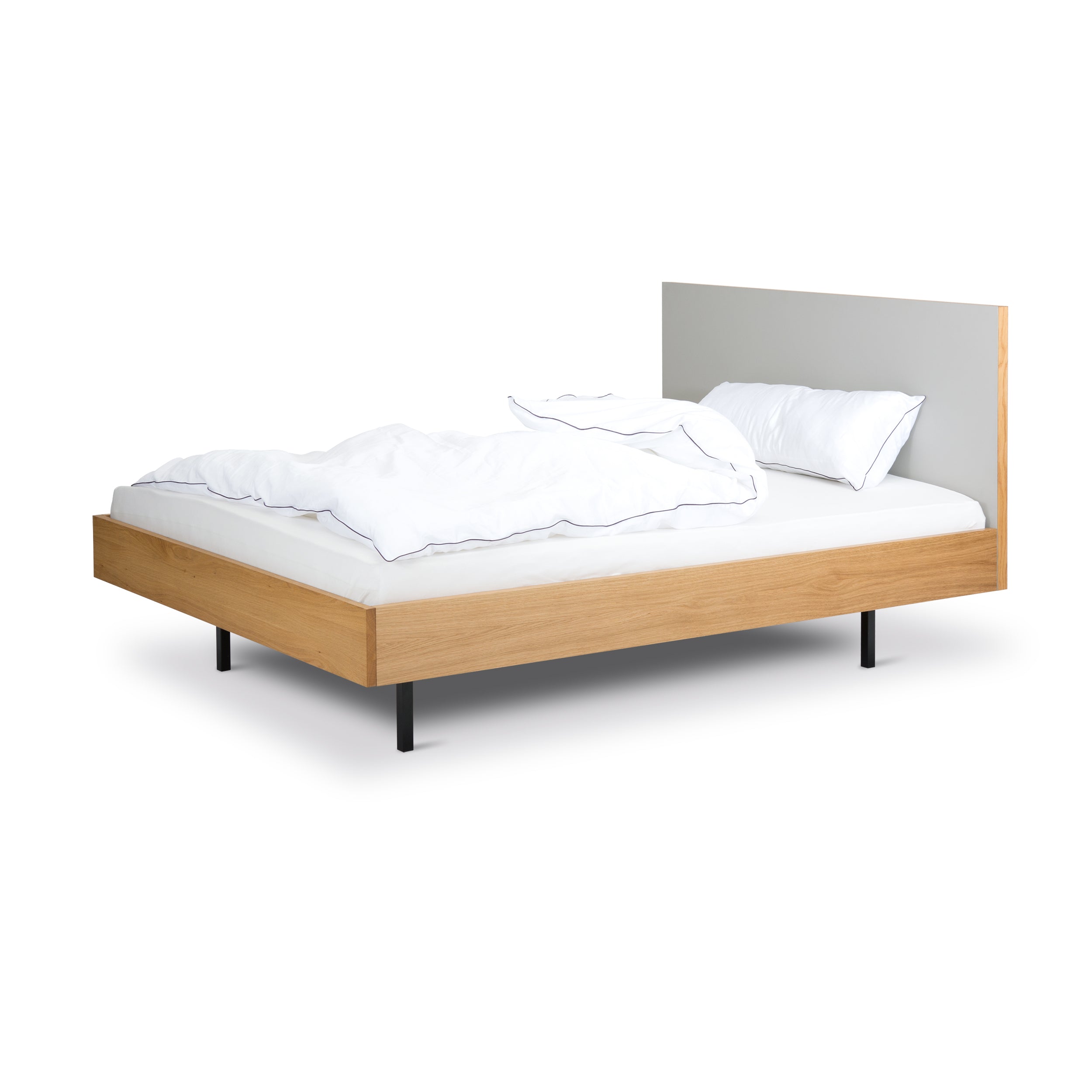 The Bartmann Berlin Unidorm Bed combines a modern, minimalist oak frame with black powder-coated steel legs. It includes a white duvet and pillow, while its simple flat headboard in a light color completes the UNIDORM aesthetic against a plain white backdrop.